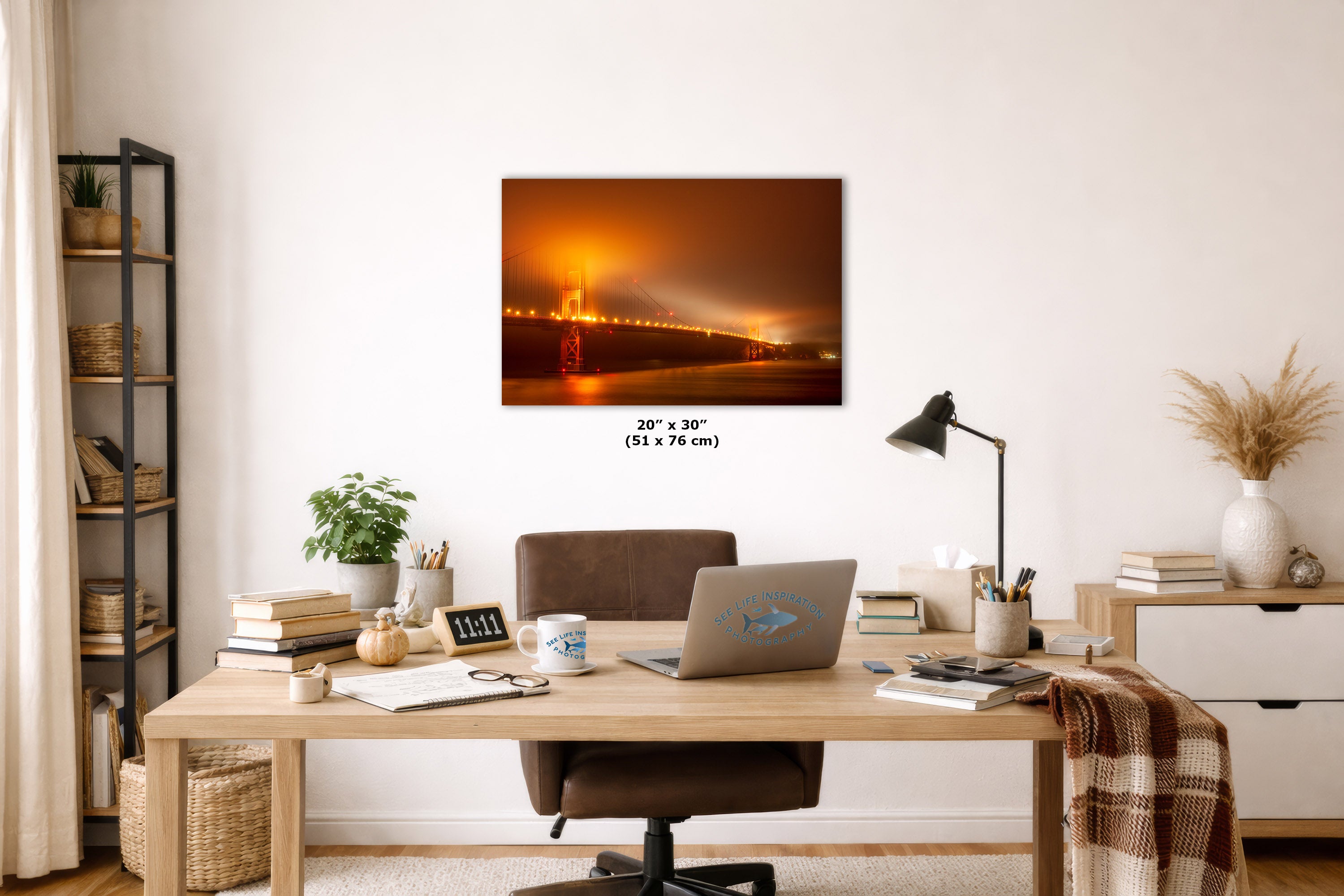 A wall art print showing a glowing orange and brown bridge scene at dusk, displayed above a wooden desk in a styled home office. The print includes size text reading 20 x 30" (51 x 76 cm).