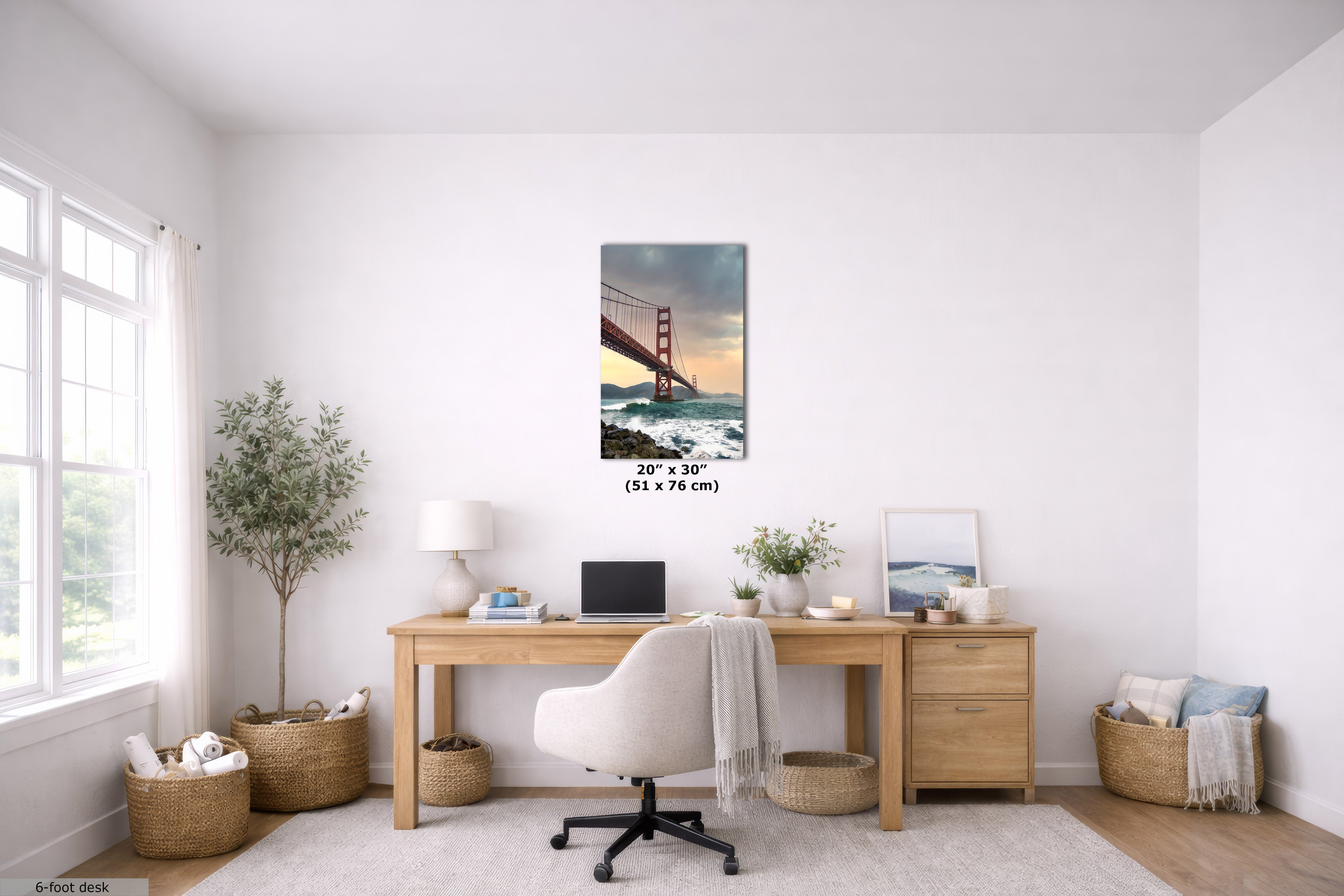 A framed vertical wall art print depicting the Golden Gate Bridge over water, displayed on a white wall above a wooden desk in a bright, modern home office. The print includes size text at the bottom indicating 20" x 30" (51 x 76 cm).