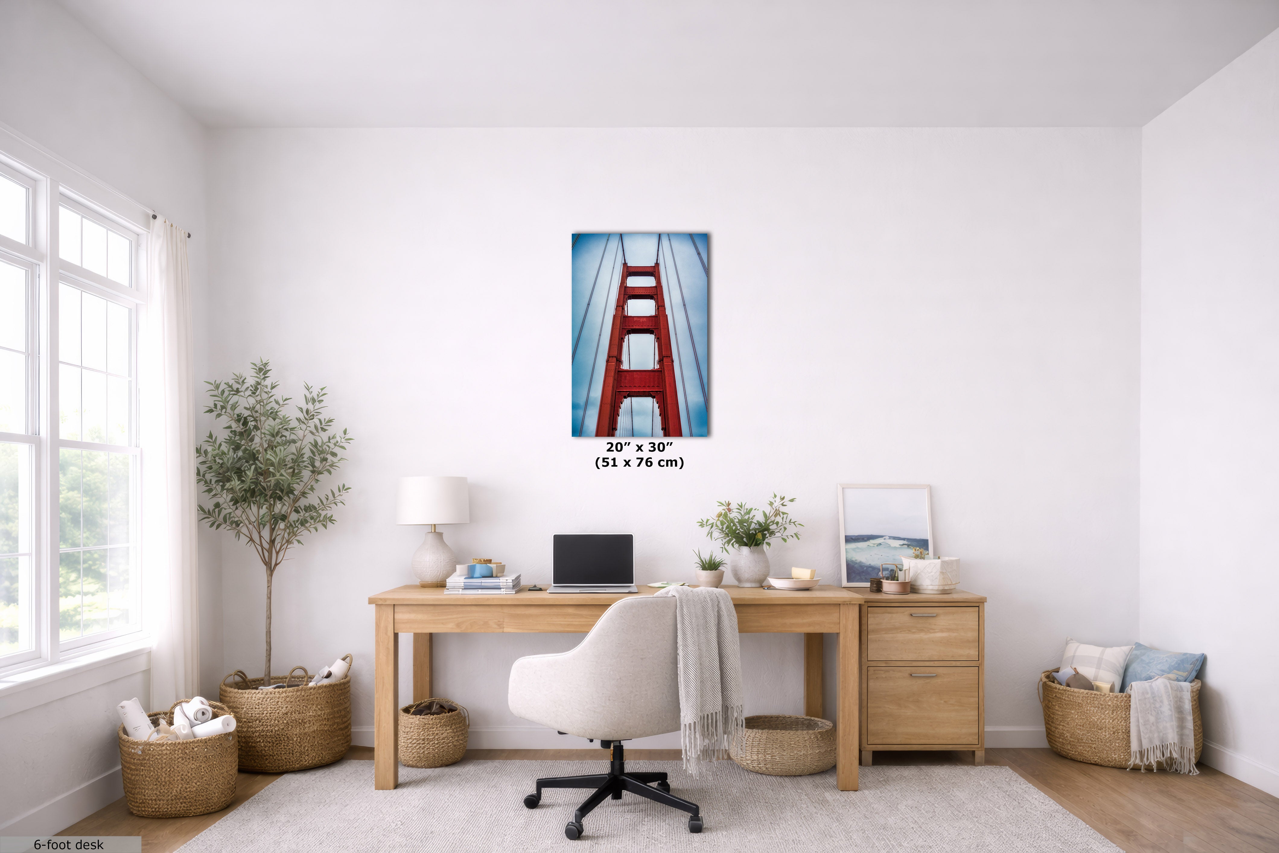 A 20 x 30 inch vertical canvas print of the Golden Gate Bridge, featuring a red bridge over blue water, displayed on a white wall in a modern, bright home office setting with a wooden desk, white chair, and plants.