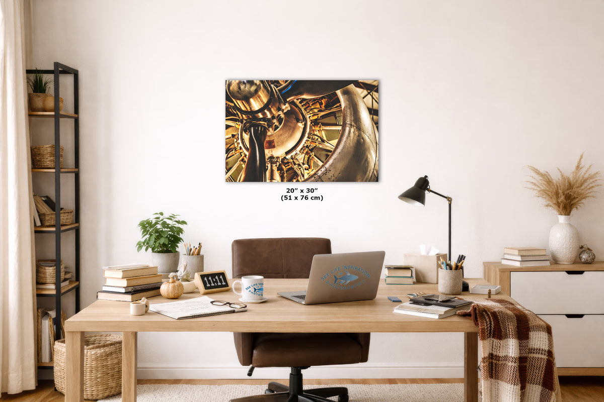 A 20 x 30 inch canvas print of a golden mechanical engine is displayed on a white wall in a modern, styled home office setting with a wooden desk, laptop, and chair.