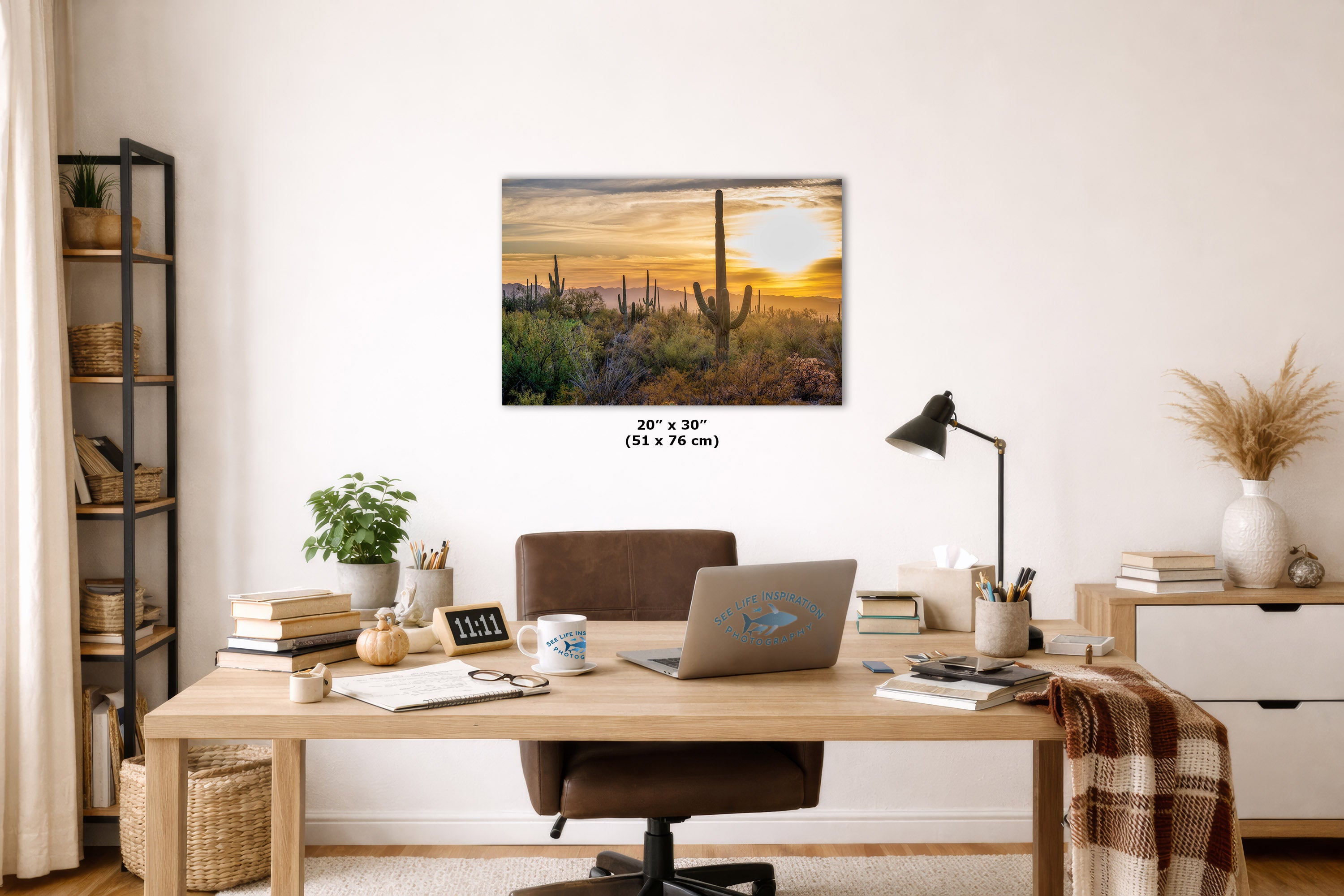 A wall art print depicting a desert sunset with saguaro cacti is displayed above a wooden desk in a modern home office setting. The print is shown with its dimensions labeled as 20 x 30 inches (51 x 76 cm) below it.