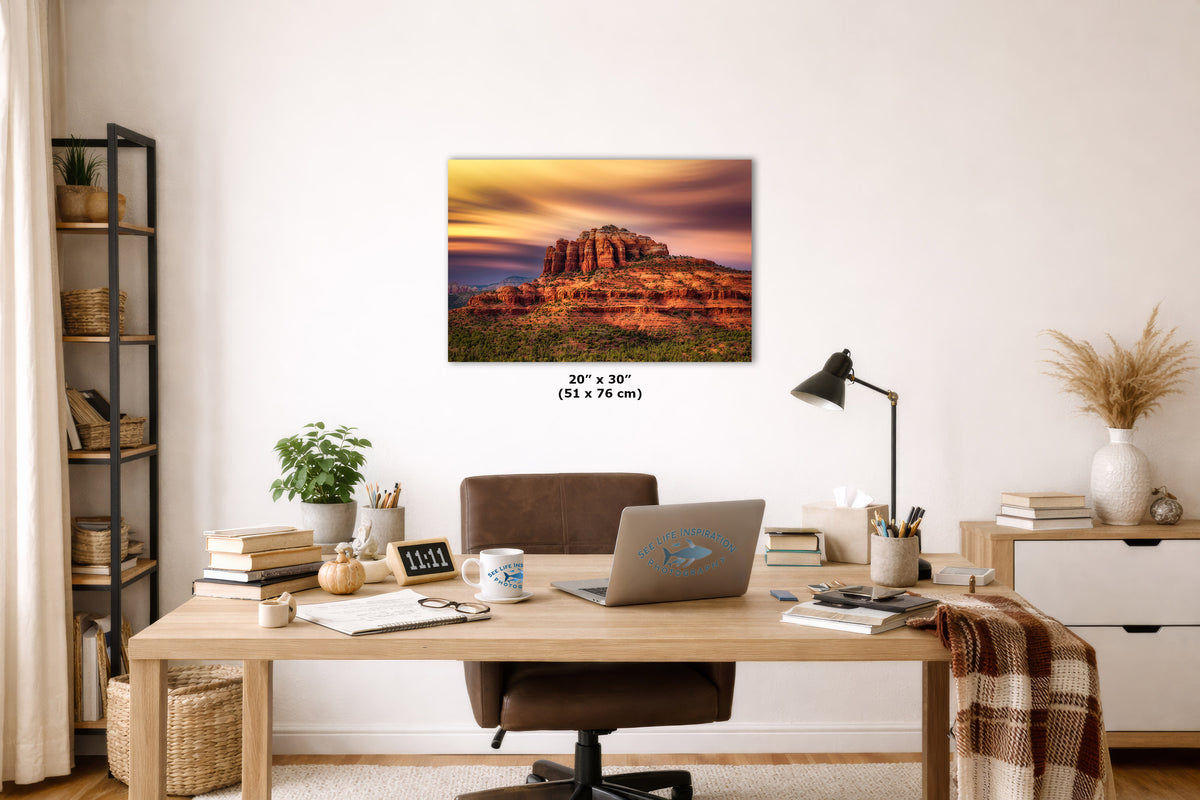 A wall art print showing a desert rock formation at sunset hangs above a wooden desk in a styled home office. The print includes size text reading 20 x 30 (51 x 76 cm).