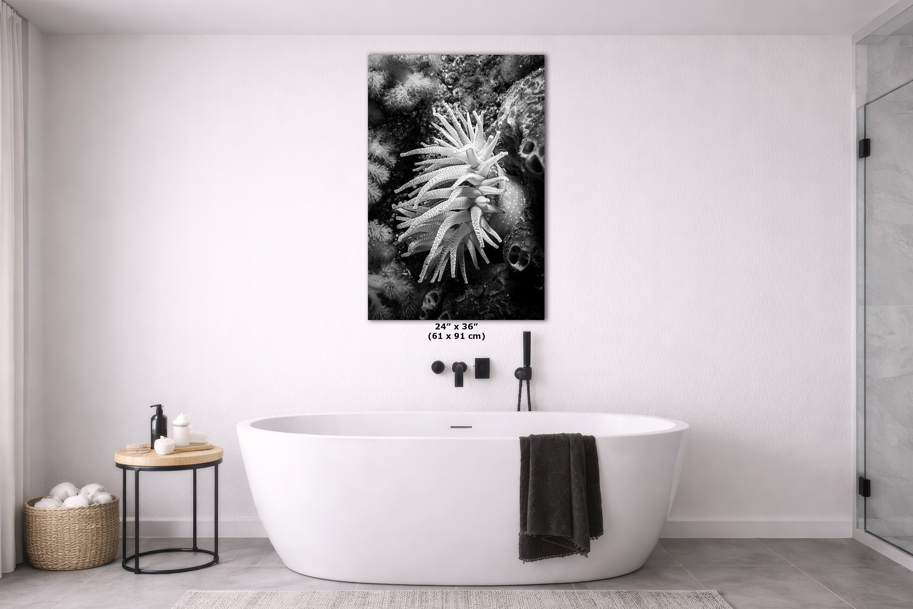 A black and white canvas wall art print of an anemone hanging above a freestanding white bathtub in a modern, minimalist bathroom.