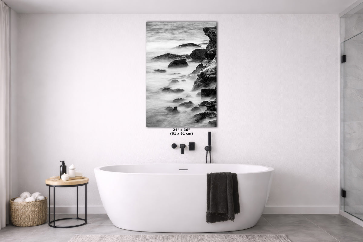 A black and white coastal landscape canvas print is displayed on a white wall above a modern freestanding bathtub in a bright, contemporary bathroom.