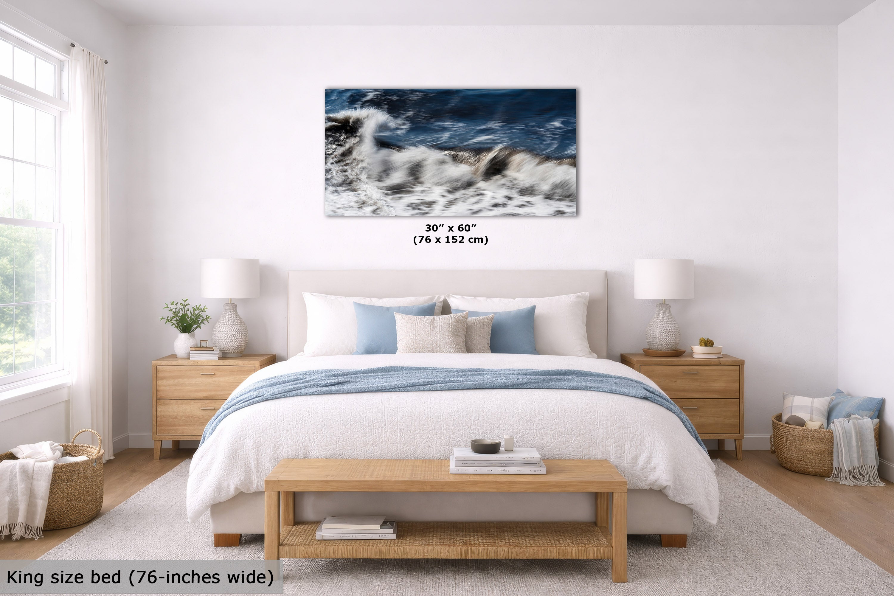A framed wall art print showing a dramatic ocean wave scene in blue, white, and gray tones, displayed above a neatly made bed in a bright, modern bedroom. The print includes size text reading 30" x 60" (76 x 152 cm).