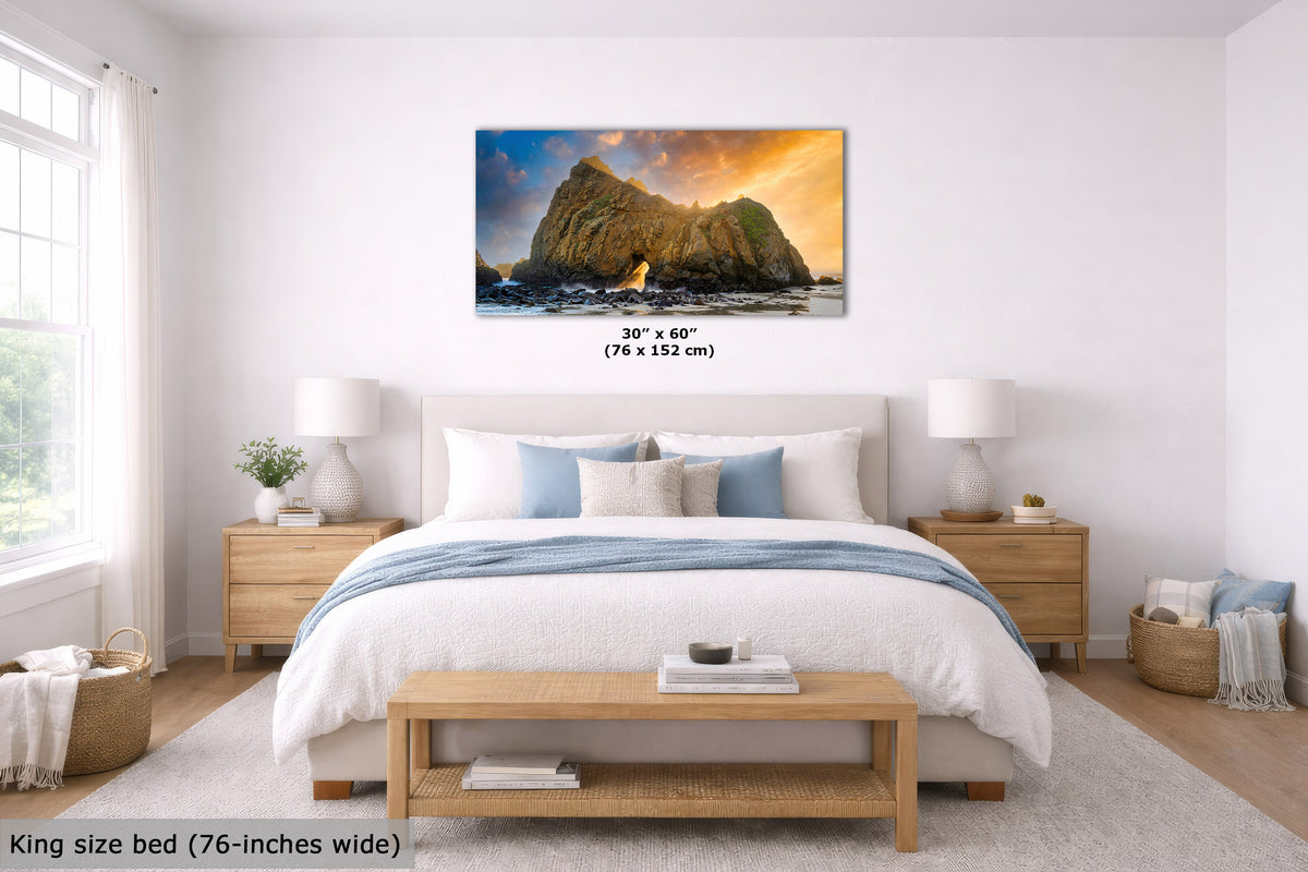A framed wall art print showing a rocky coastal scene with warm sunset light is displayed above a neatly made bed in a bright, modern bedroom. The print includes size text reading 30" x 60" (76 x 152 cm), and the room scene also notes a king size bed 76-inches wide.