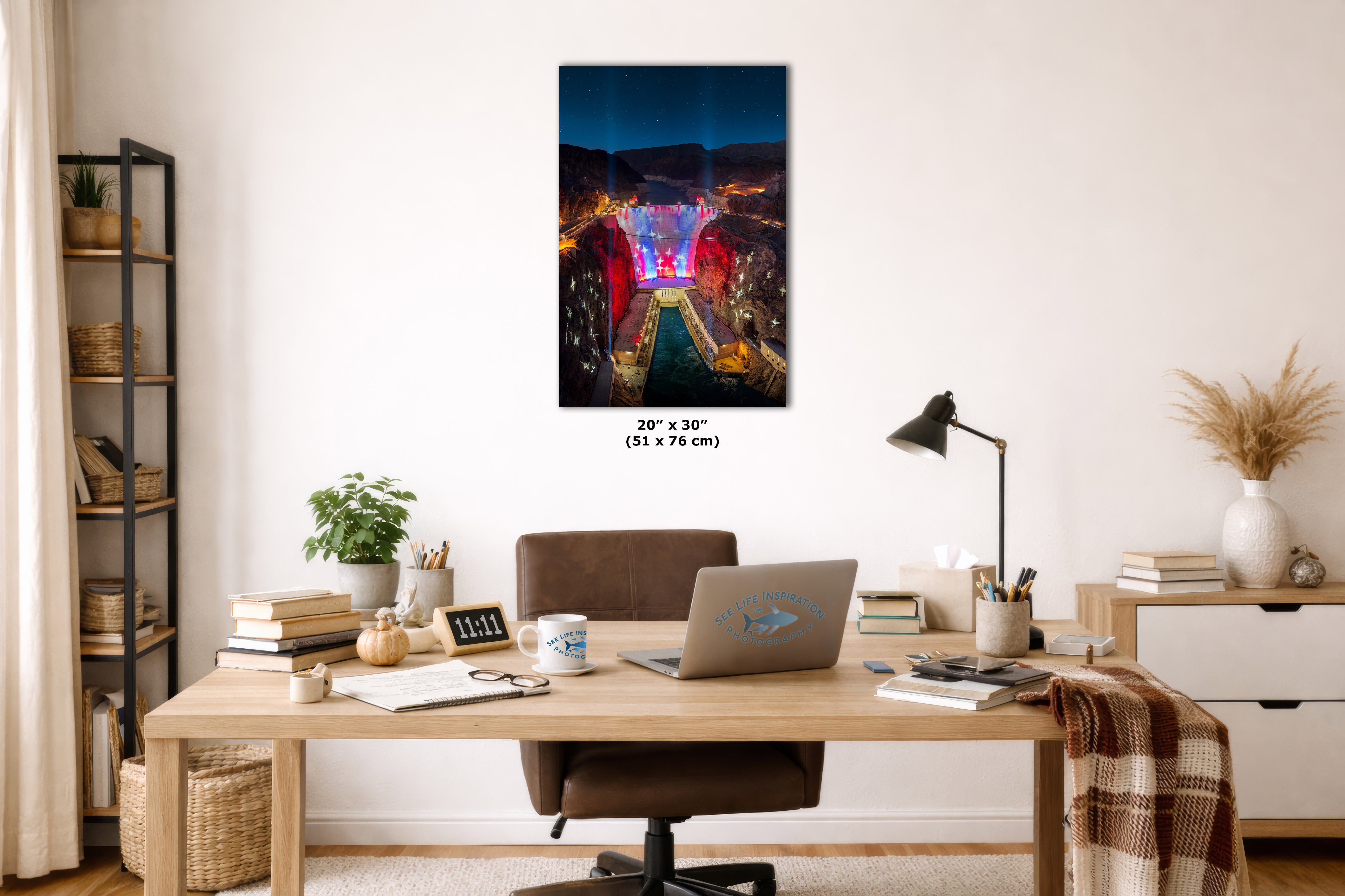 A wall art print showing a colorful city bridge at night hangs above a wooden desk in a styled home office. The print is labeled 20 x 30 inches (51 x 76 cm) and is shown in a bright, modern room setting with a desk, laptop, lamp, and shelving.