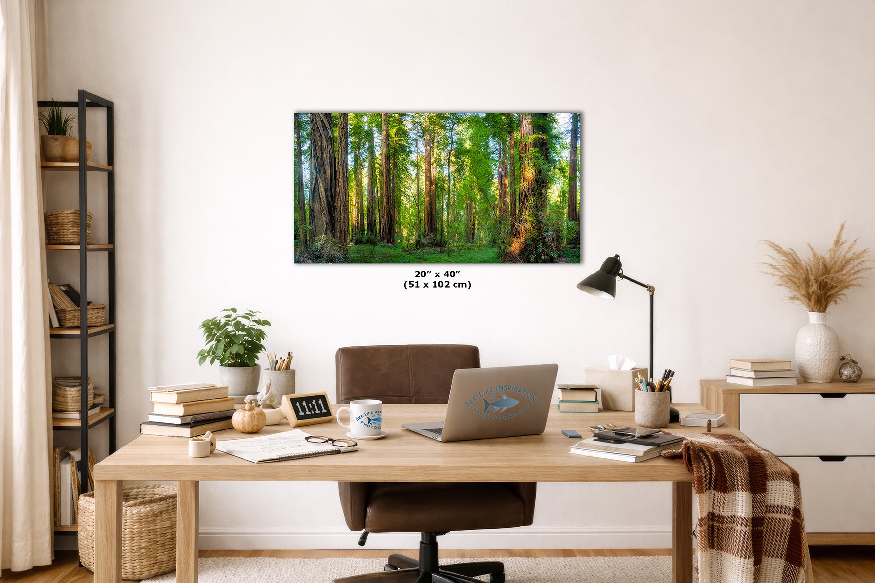 A California Redwood forest wall art print hangs above a wooden desk in a styled home office. The print shows a lush green woodland scene with tall trees and sunlight filtering through the canopy.
