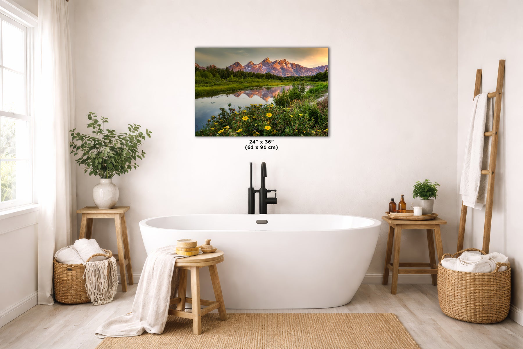 A wall art print depicting a mountain landscape with a reflective river and wildflowers, displayed above a white freestanding bathtub in a bright, neutral-toned bathroom. The print includes size text reading 24 x 36 inches (61 x 91 cm).