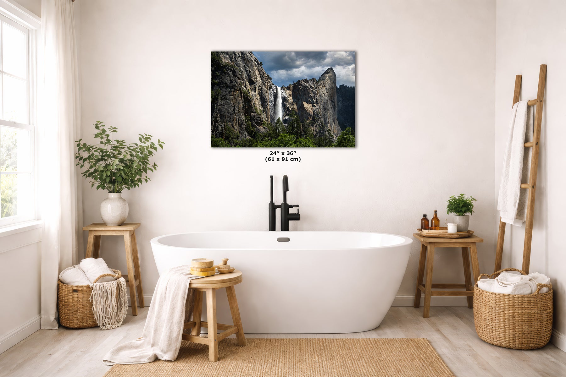 A framed wall art print depicting Yosemite's Bridalveil Waterfall between rocky cliffs, displayed above a white freestanding bathtub in a bright, neutral-toned bathroom. Small text below the print reads 24 x 36 inches.