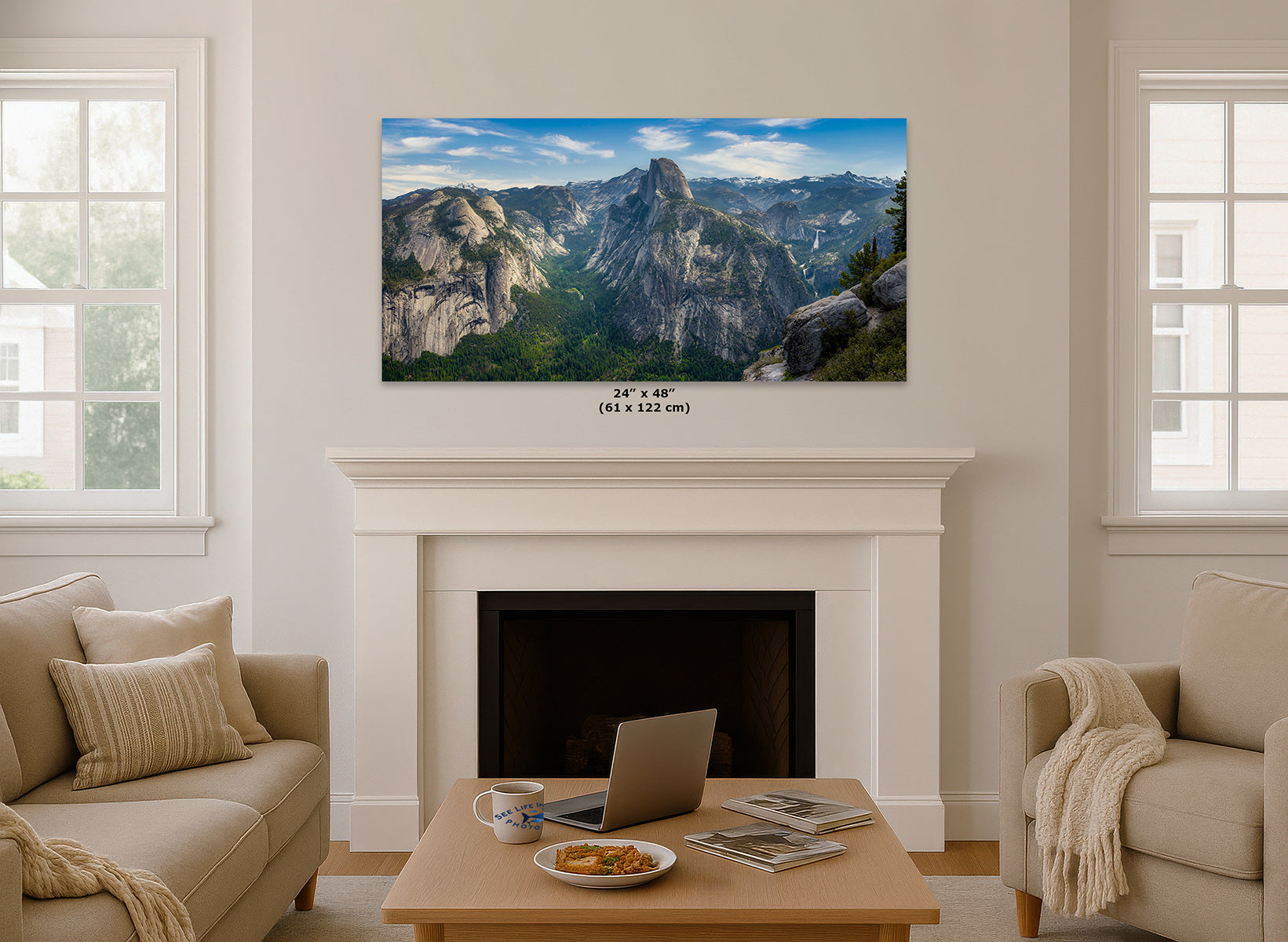 A wall art print showing a mountain landscape of Half Dome is displayed above a white fireplace in a bright living room. The print includes a small-sized label reading 24 x 48 inches (61 x 122 cm).