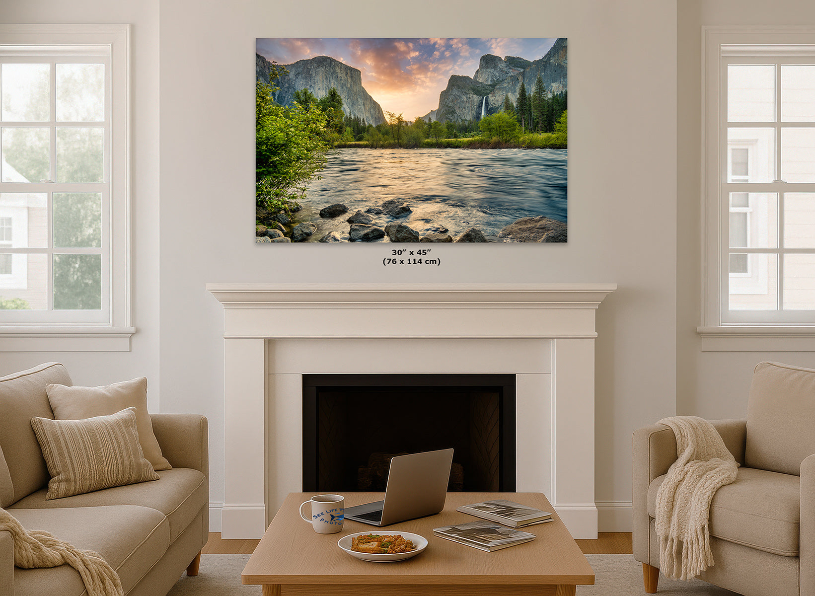 A wall art decor print of Yosemite's Valley View depicting a scenic mountain river landscape with a sunset sky, displayed above a white fireplace mantel in a bright living room. Small text below the print reads 30 x 45 in (76 x 114 cm).