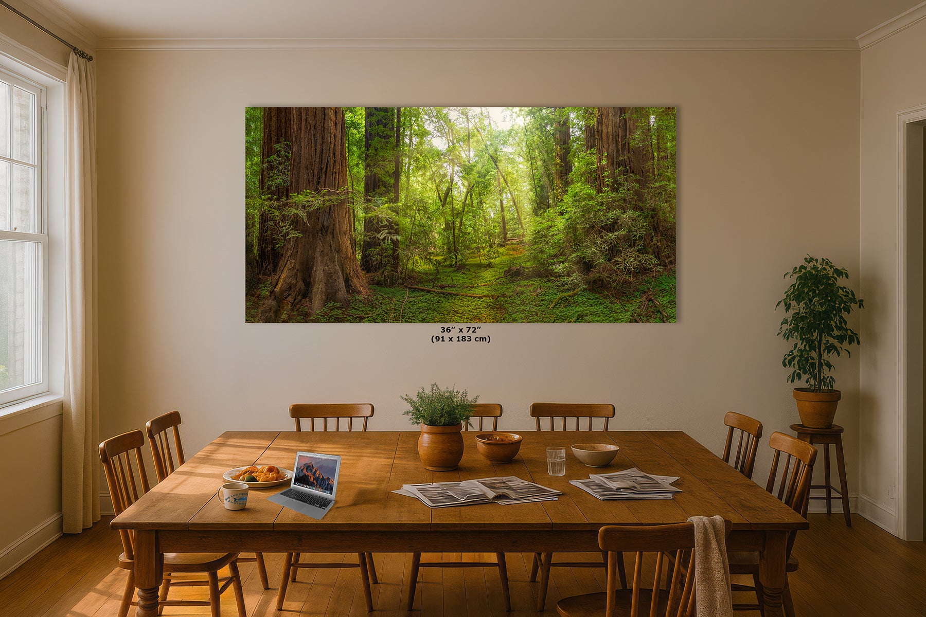 A large rectangular wall art print depicting a lush green forest path with tall Redwood trees, displayed above a wooden dining table in a warm, modern dining room. Small text below the print reads '36" x 72" (91 x 183 cm)'.