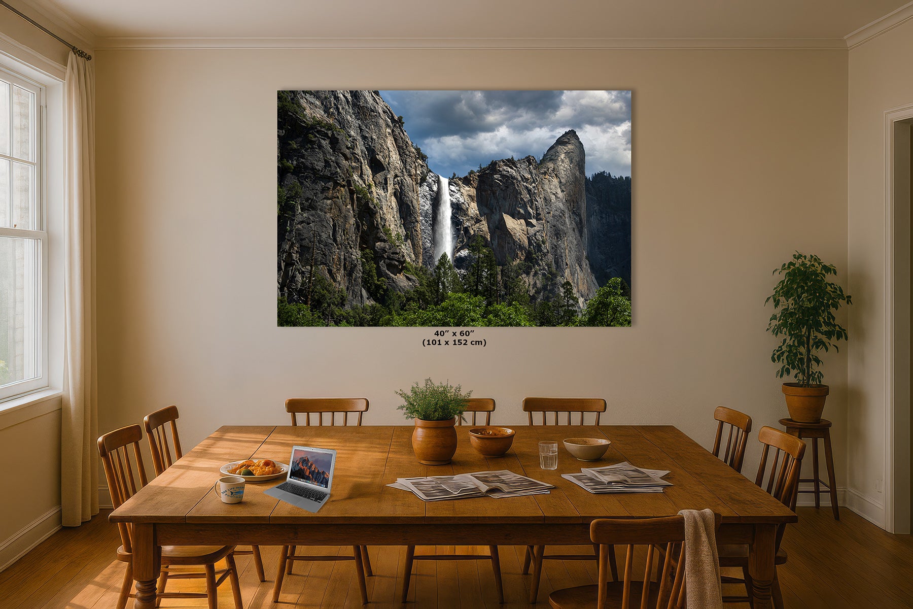 A large wall art print depicting Yosemite's Bridalveil waterfall between rocky cliffs hangs on a beige dining room wall above a wooden table with chairs, plants, and breakfast items.