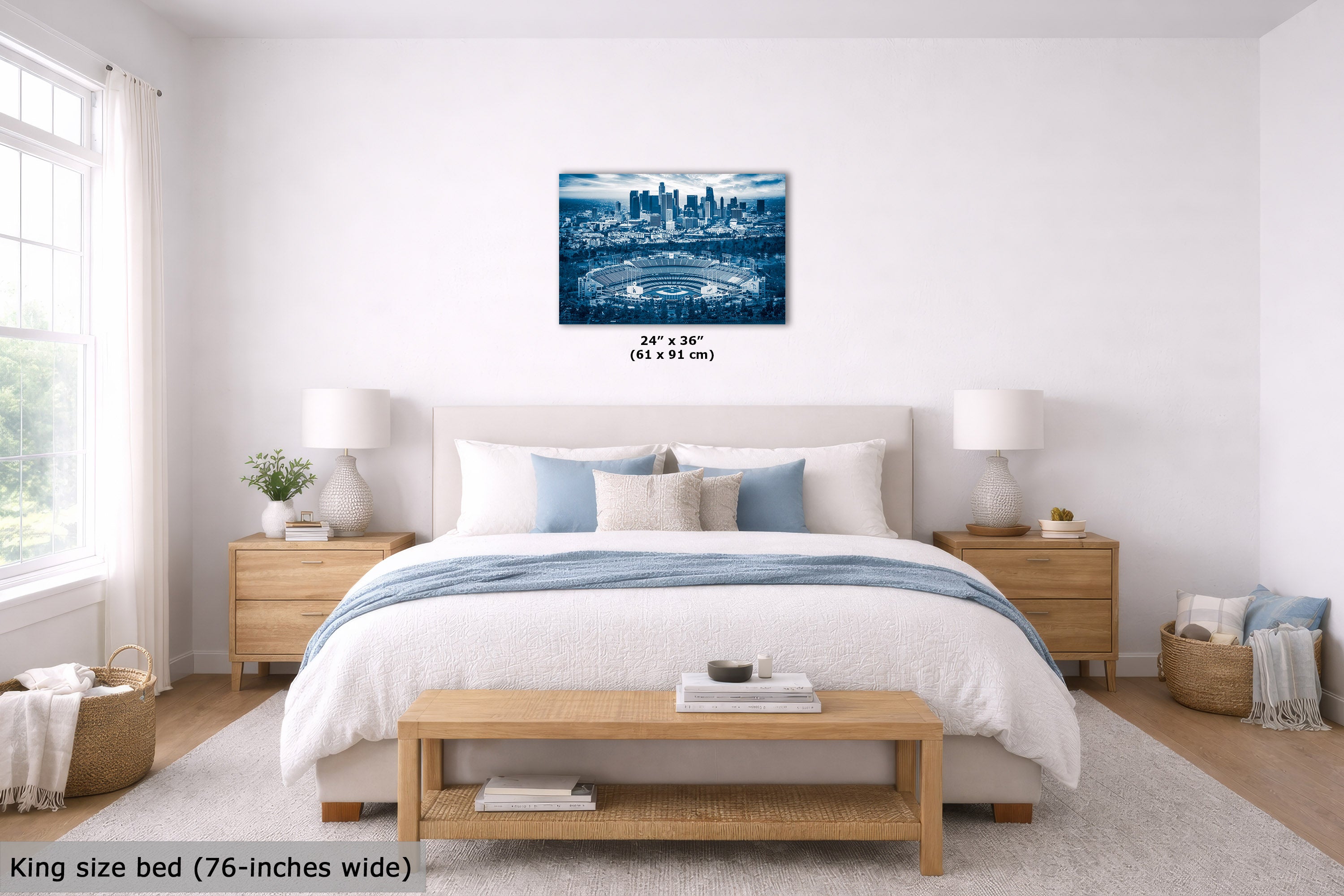 A blue-toned city skyline wall art print displayed above a neatly made bed in a bright, modern bedroom. The print is shown as a rectangular canvas with dimensions labeled below it, and the room includes matching wood nightstands, white lamps, a light rug, and a wooden bench at the foot of the bed.