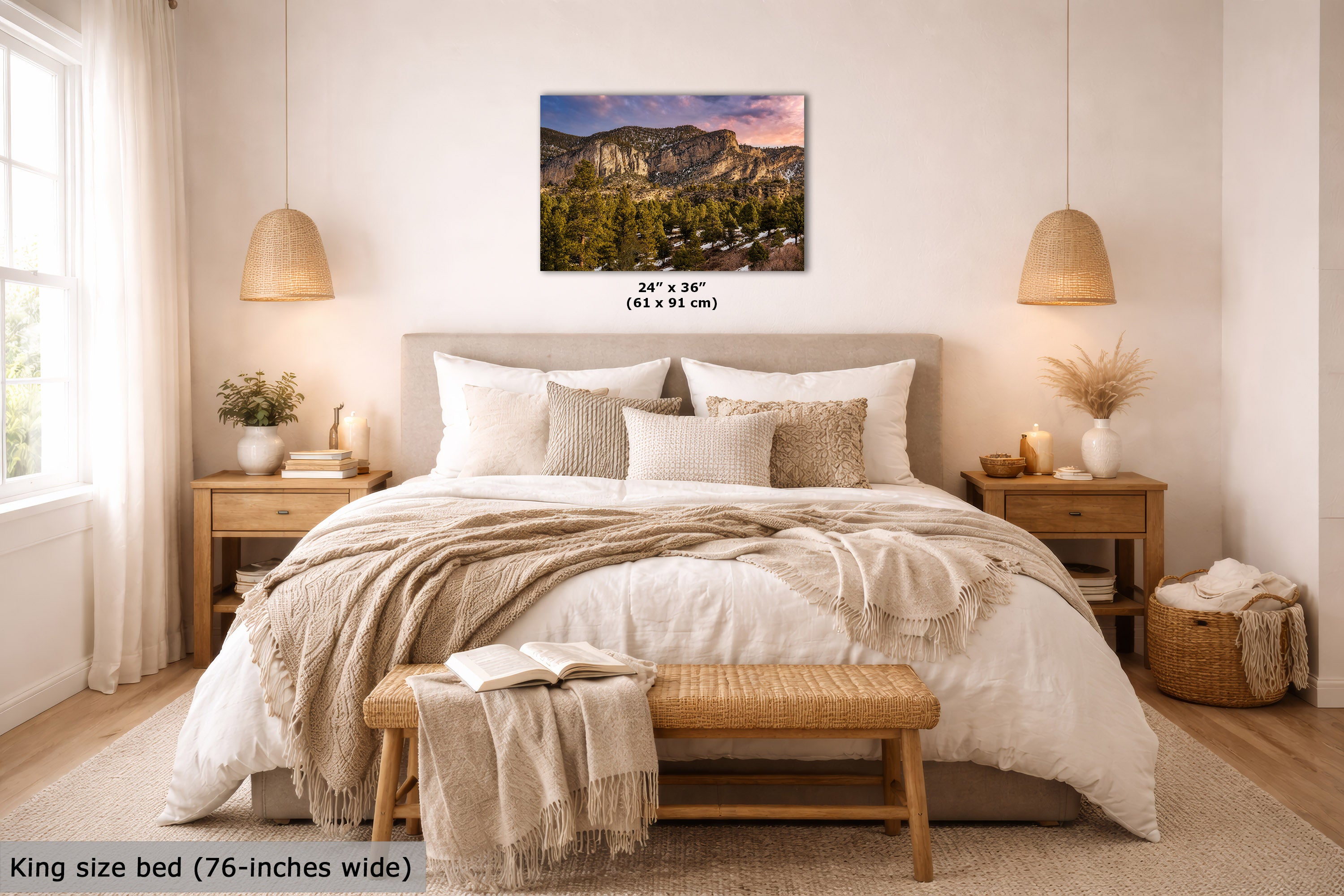 A mountain landscape wall art print is displayed above a neatly made bed in a bright, modern bedroom. The print shows a scenic mountain range with green forests and a colorful sunset sky.