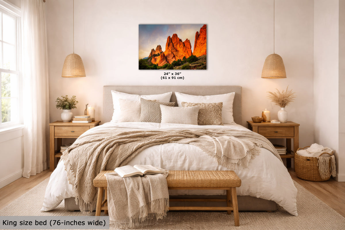 A wall art print showing bright orange rock formations at sunrise is displayed above a neatly made bed in a bright, modern bedroom. The print includes size text reading 24 x 36 inches (61 x 91 cm).