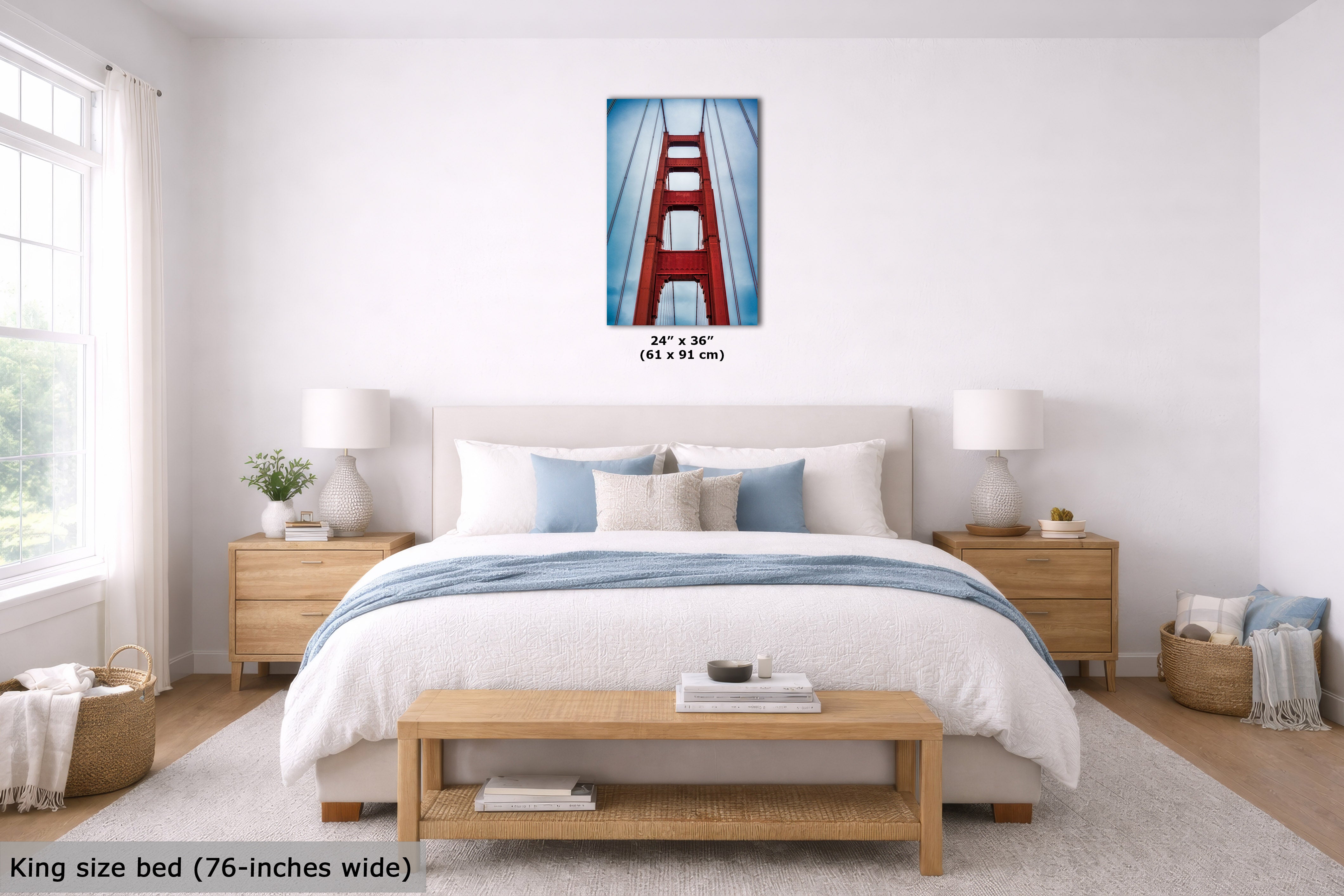A bedroom mockup featuring a vertical canvas print of the Golden Gate Bridge centered above a bed. The print has a blue sky background with the iconic red-orange bridge.