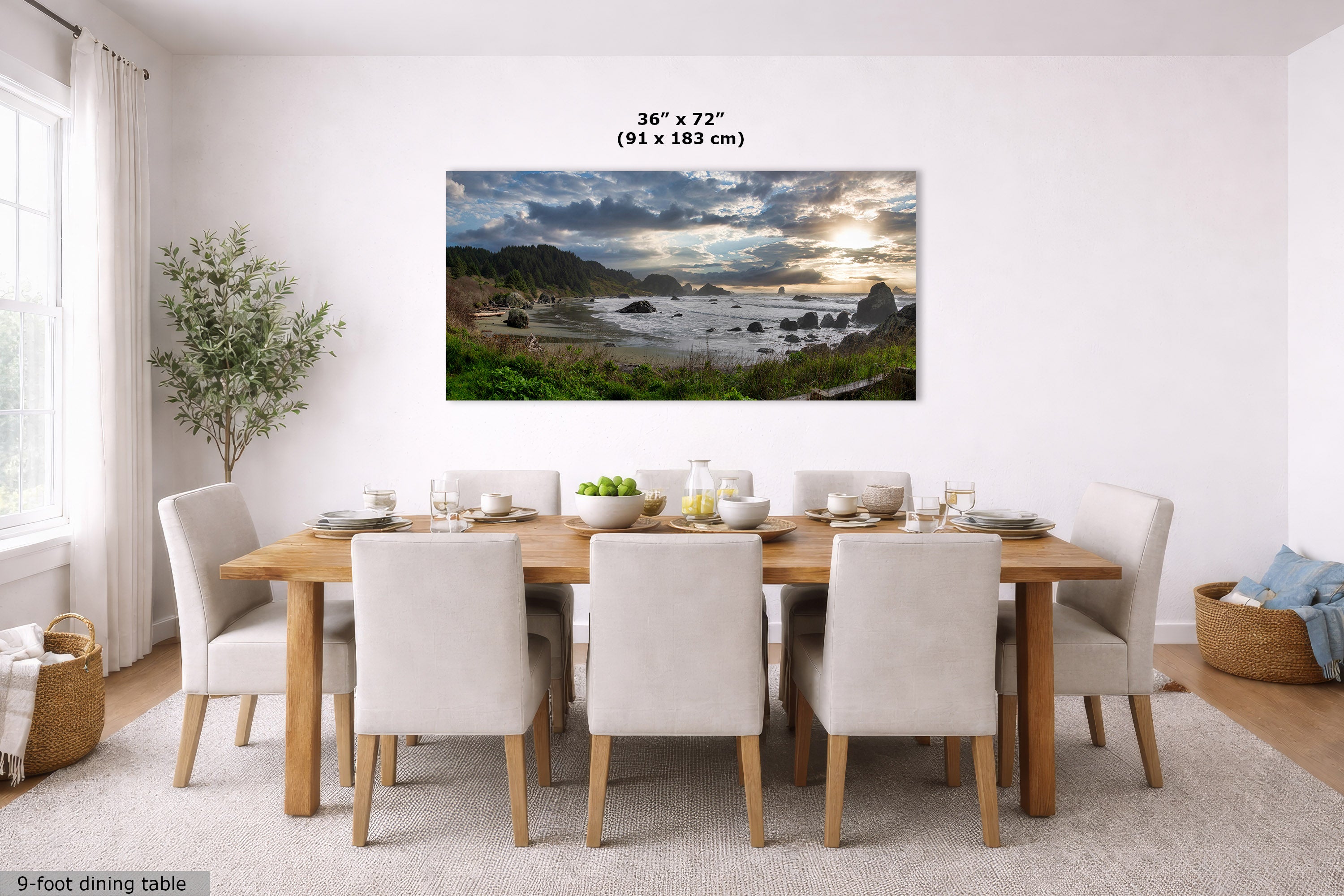 A large rectangular wall art print showing a dramatic coastal landscape with rocky cliffs, ocean waves, and a cloudy sky, displayed above a wooden dining table with white upholstered chairs in a bright dining room. Text above the print reads 36 x 72 in (91 x 183 cm).