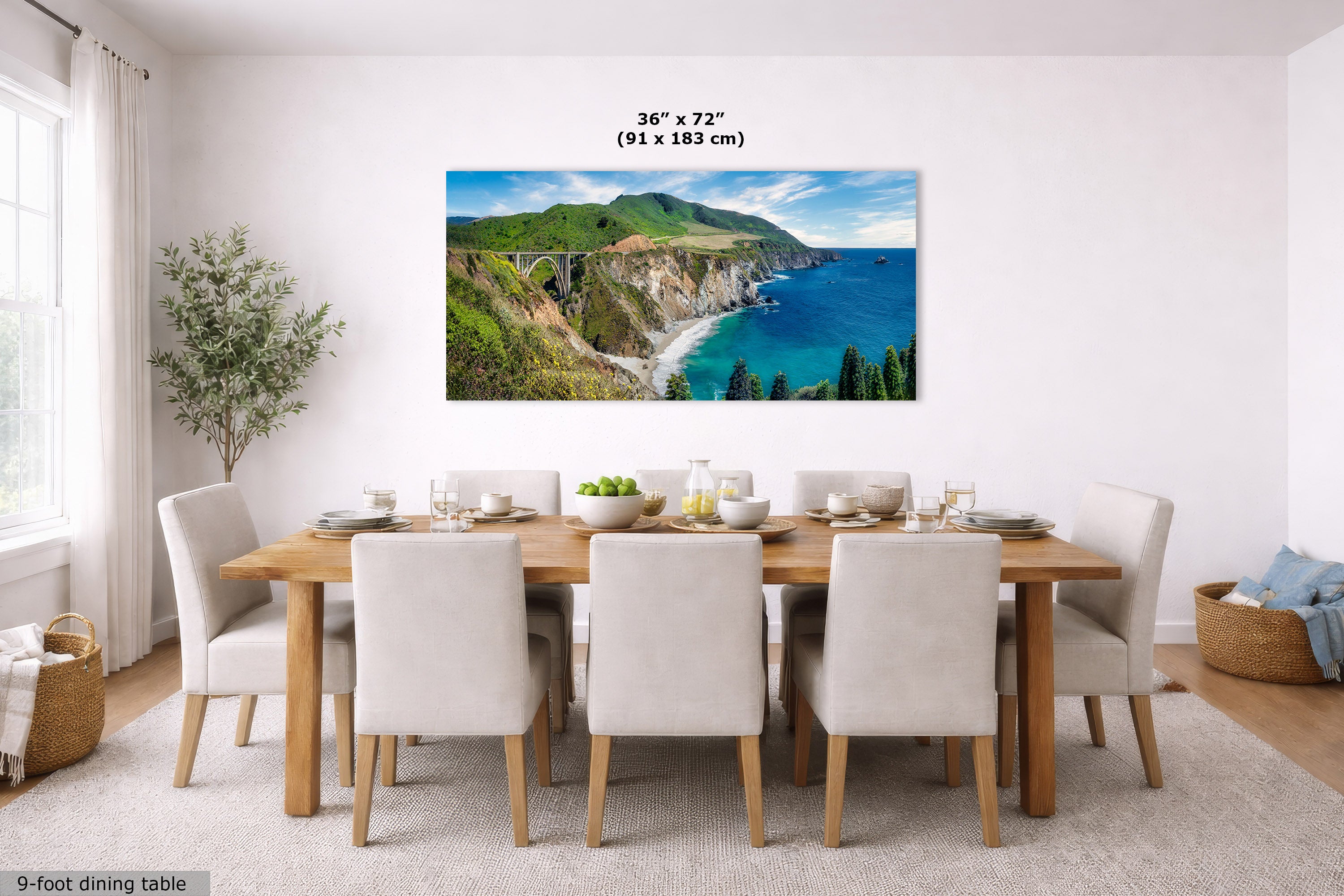 A large landscape wall art print showing a coastal cliff and blue ocean, displayed above a wooden dining table with white chairs in a bright dining room. The print includes size text reading 36 x 72 inches (91 x 183 cm).