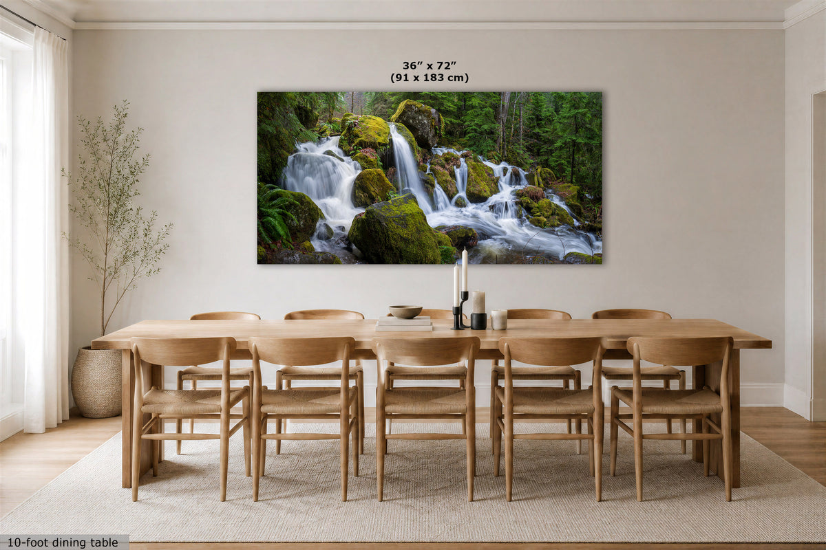 A large wall art print depicting a lush green forest waterfall, displayed in a modern dining room setting above a wooden dining table and chairs. The dimensions '36" x 72" (91 x 183 cm)' are printed directly above the artwork.
