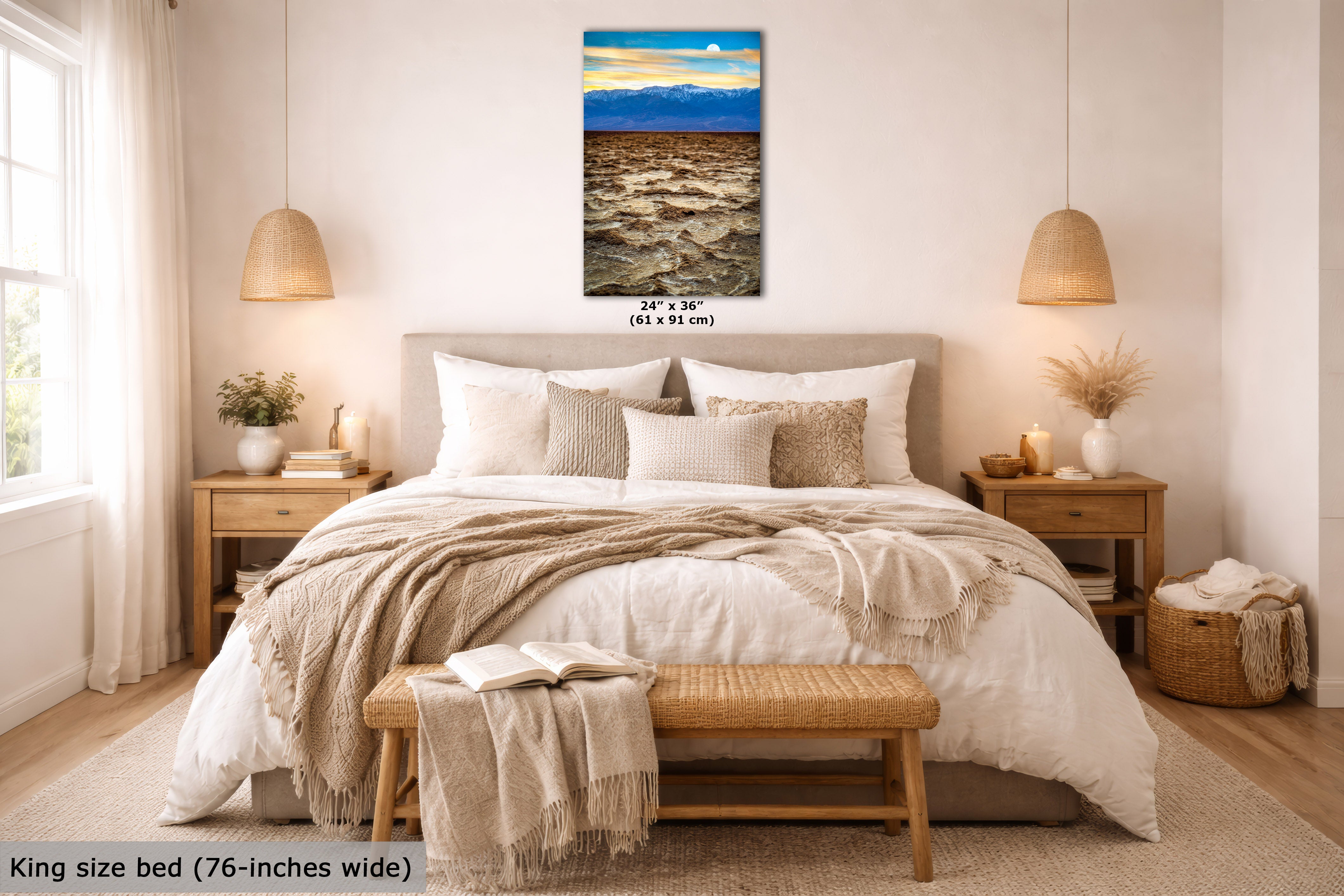 A framed wall art print showing a desert landscape with mountains and a blue sky, displayed above a neatly made bed in a bright, modern bedroom. The print includes size text reading 24 x 36 inches (61 x 91 cm).