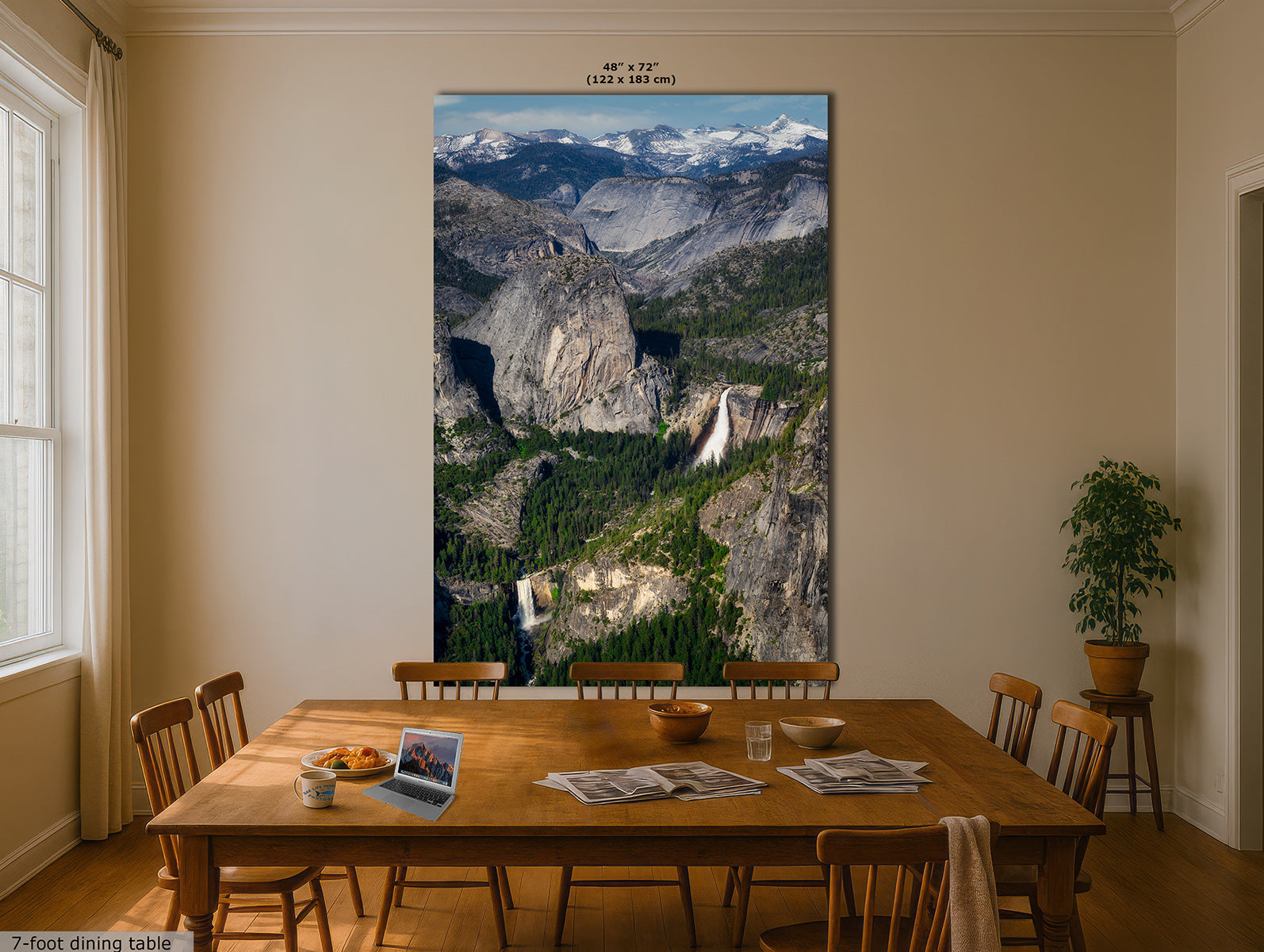 A large vertical Yosemite wall art print depicting a mountain valley landscape with snowy peaks, rocky cliffs, Nevada and Vernal waterfalls, displayed above a wooden dining table in a beige dining room. The print includes size text at the top and a small text label at the bottom left.