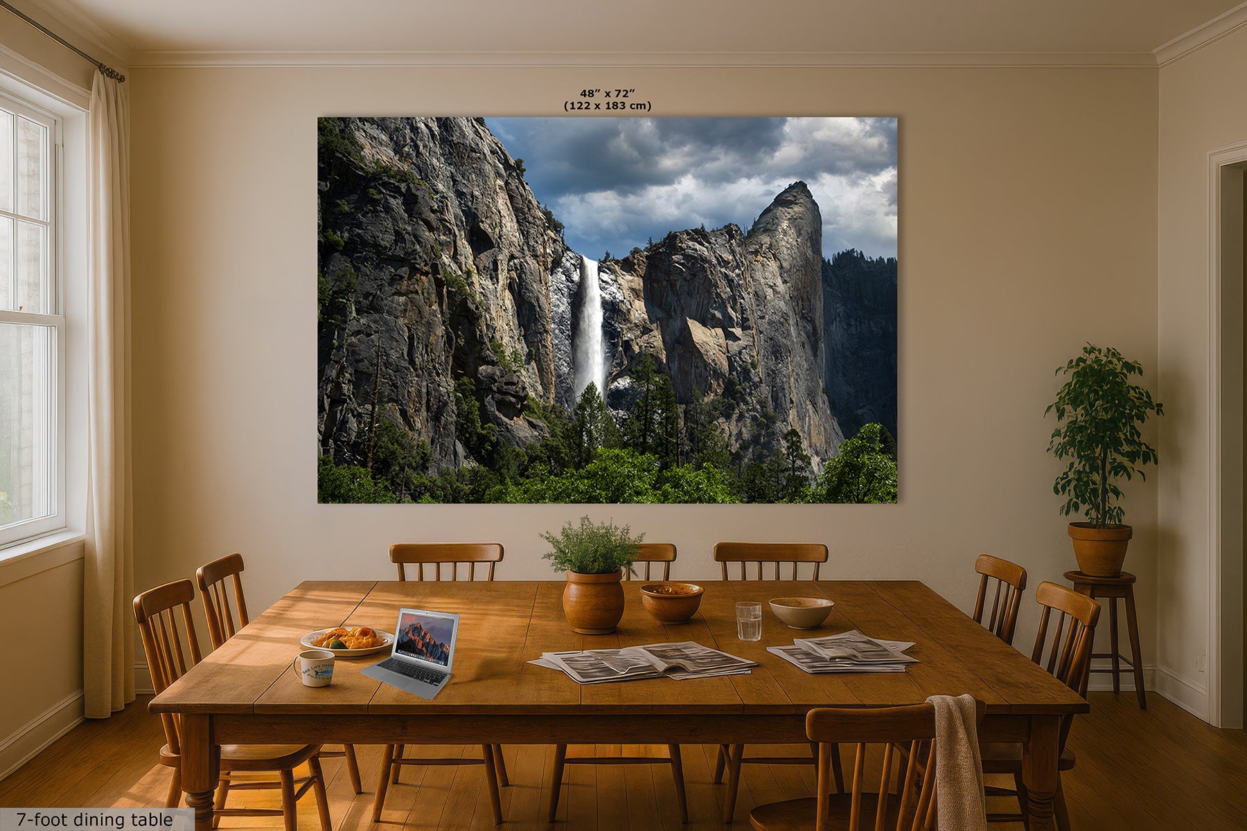 A large rectangular wall art print showing Yosemite's Bridalveil waterfall between rocky cliffs hangs above a wooden dining table in a beige dining room. The print includes small-sized text at the top and a small label at the bottom left reading 7-foot dining table.