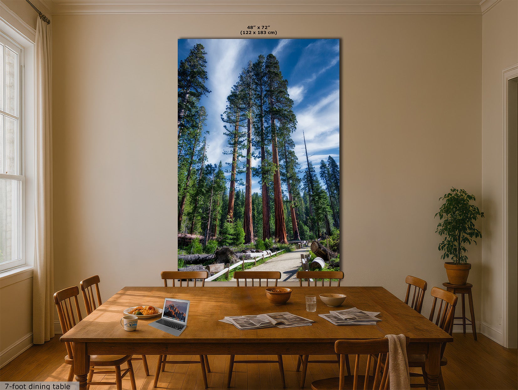 A large vertical wall art print depicting a Giant Sequoia forest of tall redwood trees under a blue sky, displayed on a beige wall above a wooden dining table in a dining room setting.