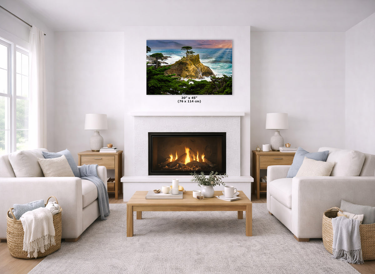 A coastal landscape wall art print of the Lone Cypress in Monterey, California, that hangs above a white fireplace in a bright, modern living room with two cream sofas, a wooden coffee table, and woven baskets.