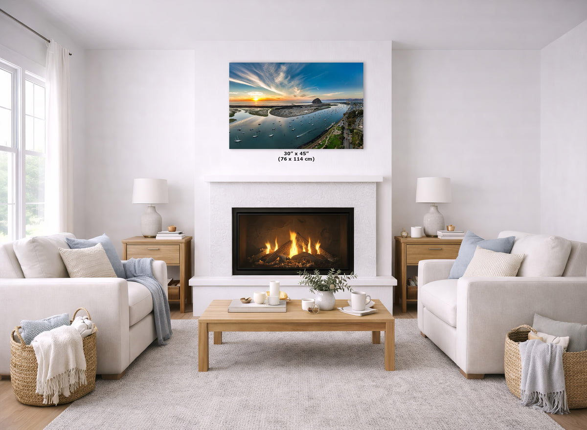 A landscape art print of a sunset over water hangs above a white fireplace in a bright, modern living room with two cream sofas, a wooden coffee table, and a light rug.