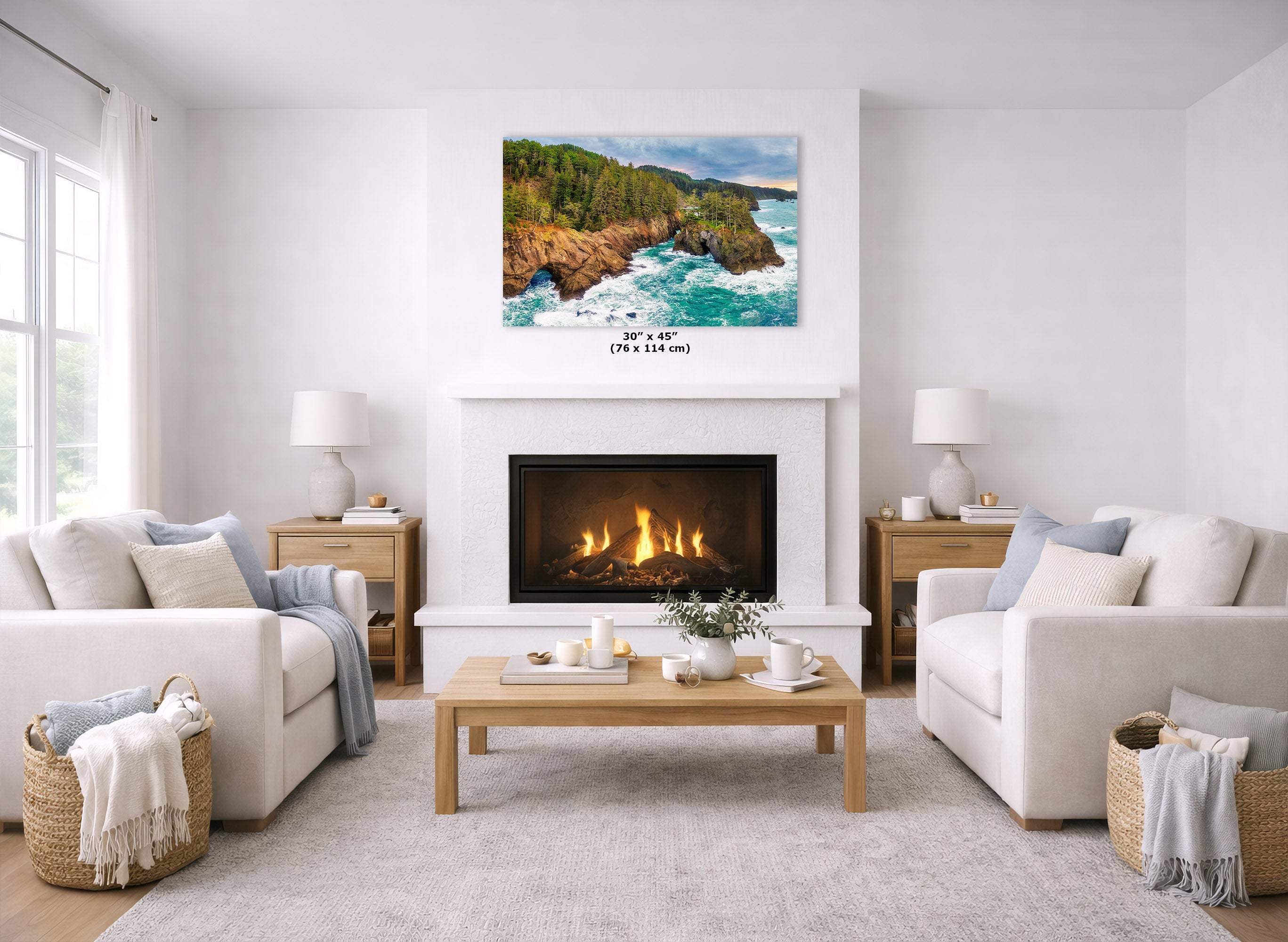 A coastal landscape wall art print hangs above a fireplace in a bright, modern living room. The artwork shows turquoise ocean water crashing onto rocky cliffs with green trees and blue sky.