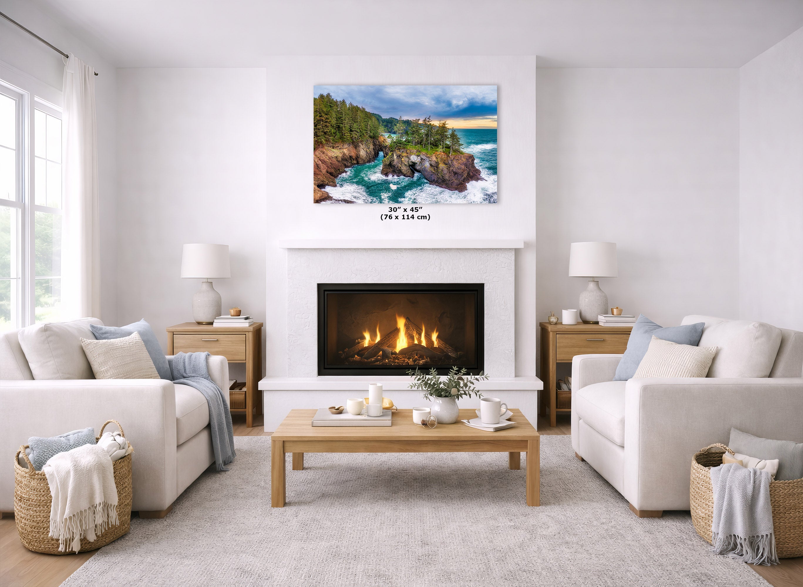 A coastal landscape art print hangs above a white fireplace in a bright, modern living room with two cream sofas, a wooden coffee table, and a light rug. The print depicts turquoise water, rocky cliffs, and green trees under a blue sky.