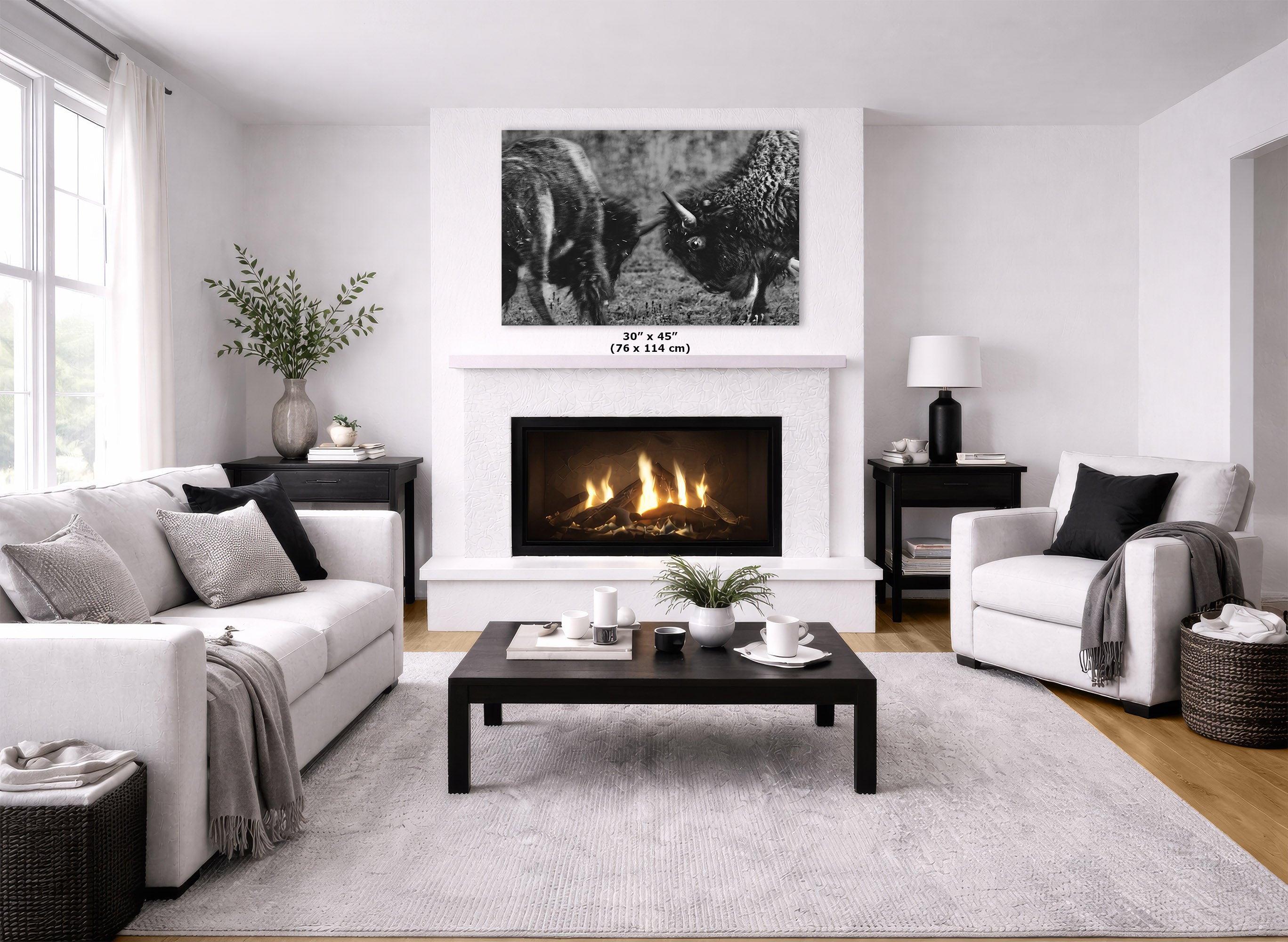 A black and white bison art print displayed on a white wall above a fireplace in a modern, bright living room with white sofas and a dark coffee table.
