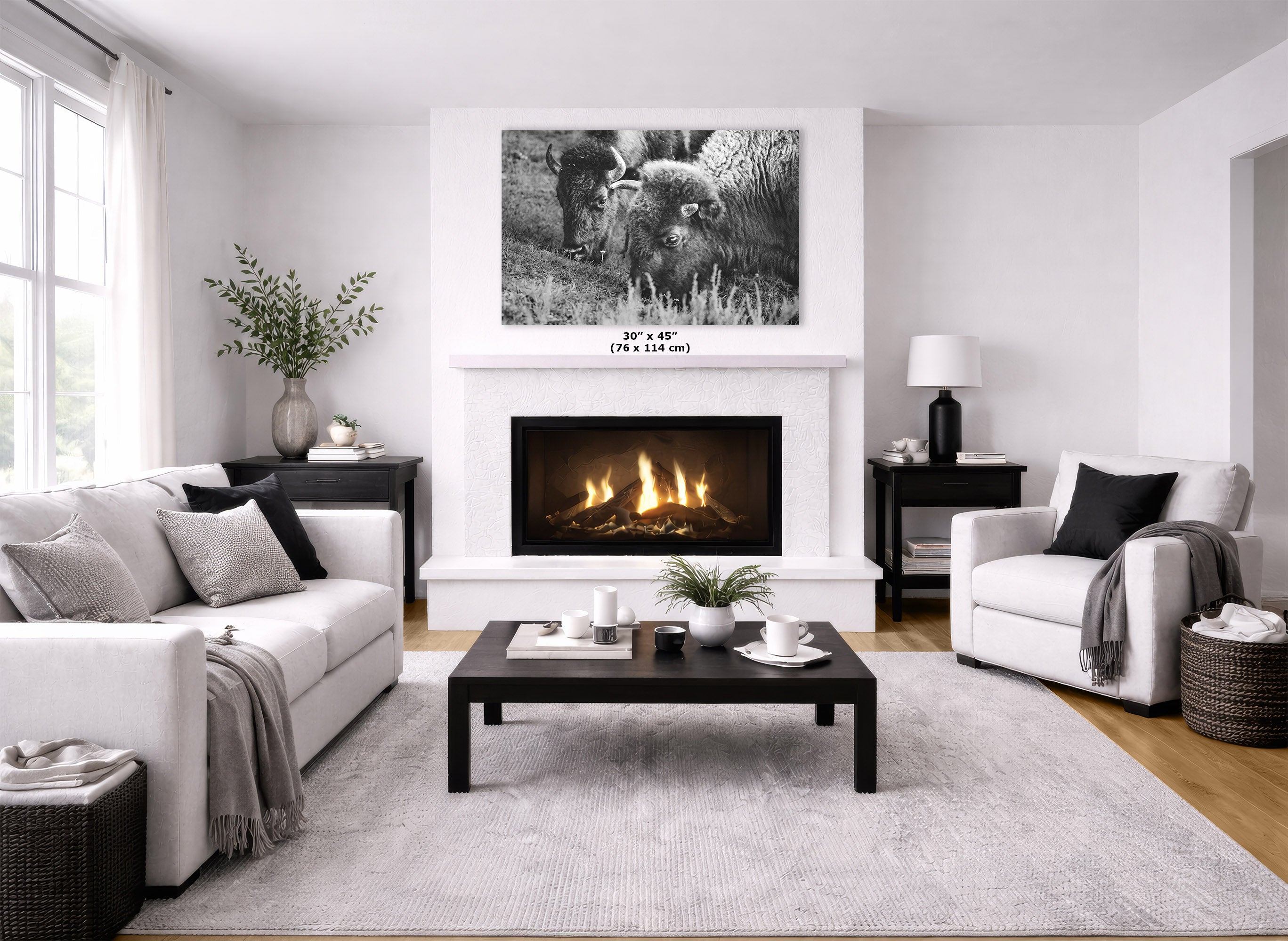 A black and white art print displayed in a modern living room setting above a white fireplace mantel, with a fire burning inside. The room features a white sofa, a white accent chair, a dark wood coffee table, and a light gray textured rug.