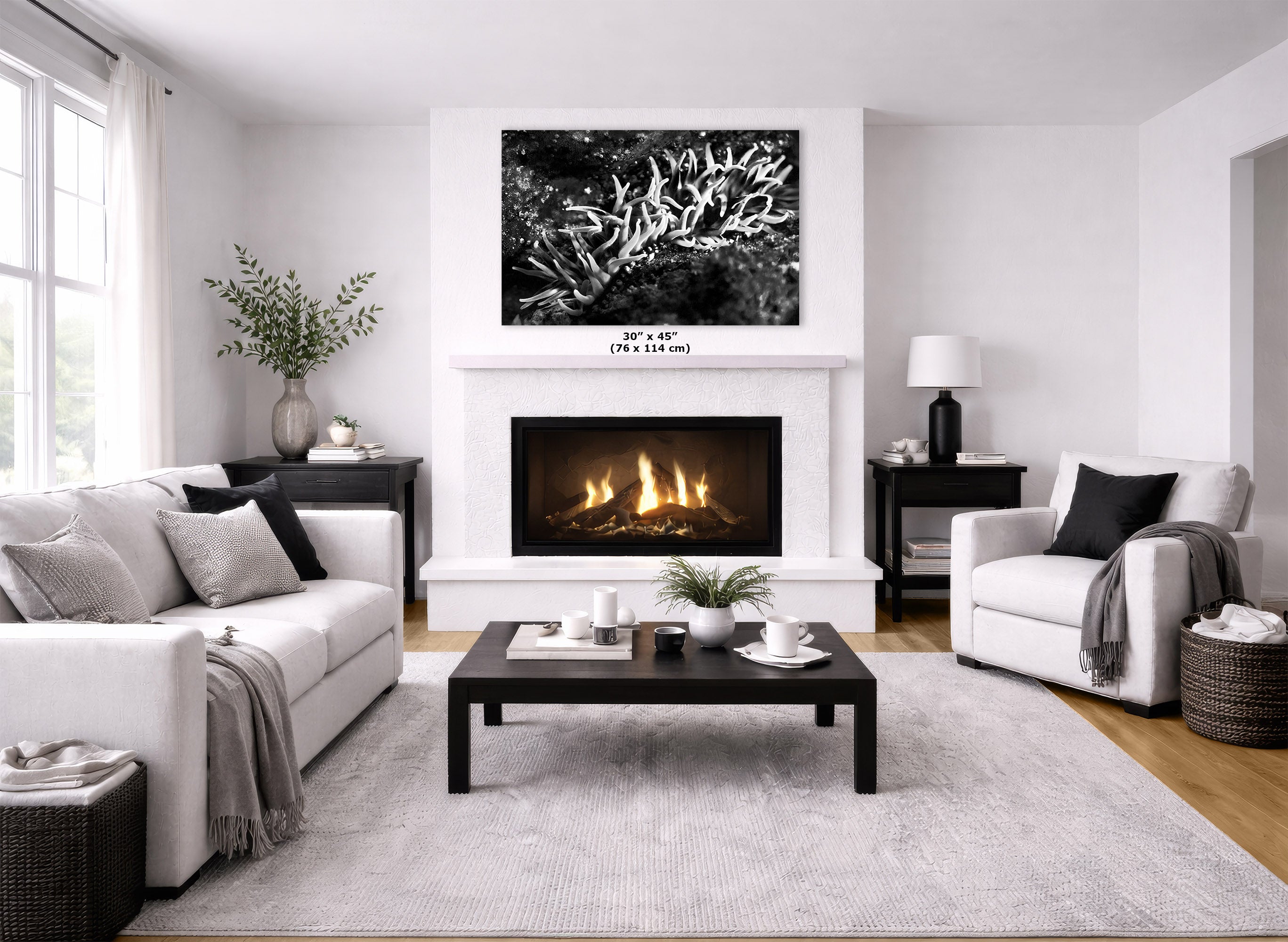 A modern living room featuring a white fireplace with a black-framed fire, a large black and white abstract canvas print above it, a white sofa, a white armchair, and a dark wood coffee table on a light gray rug.