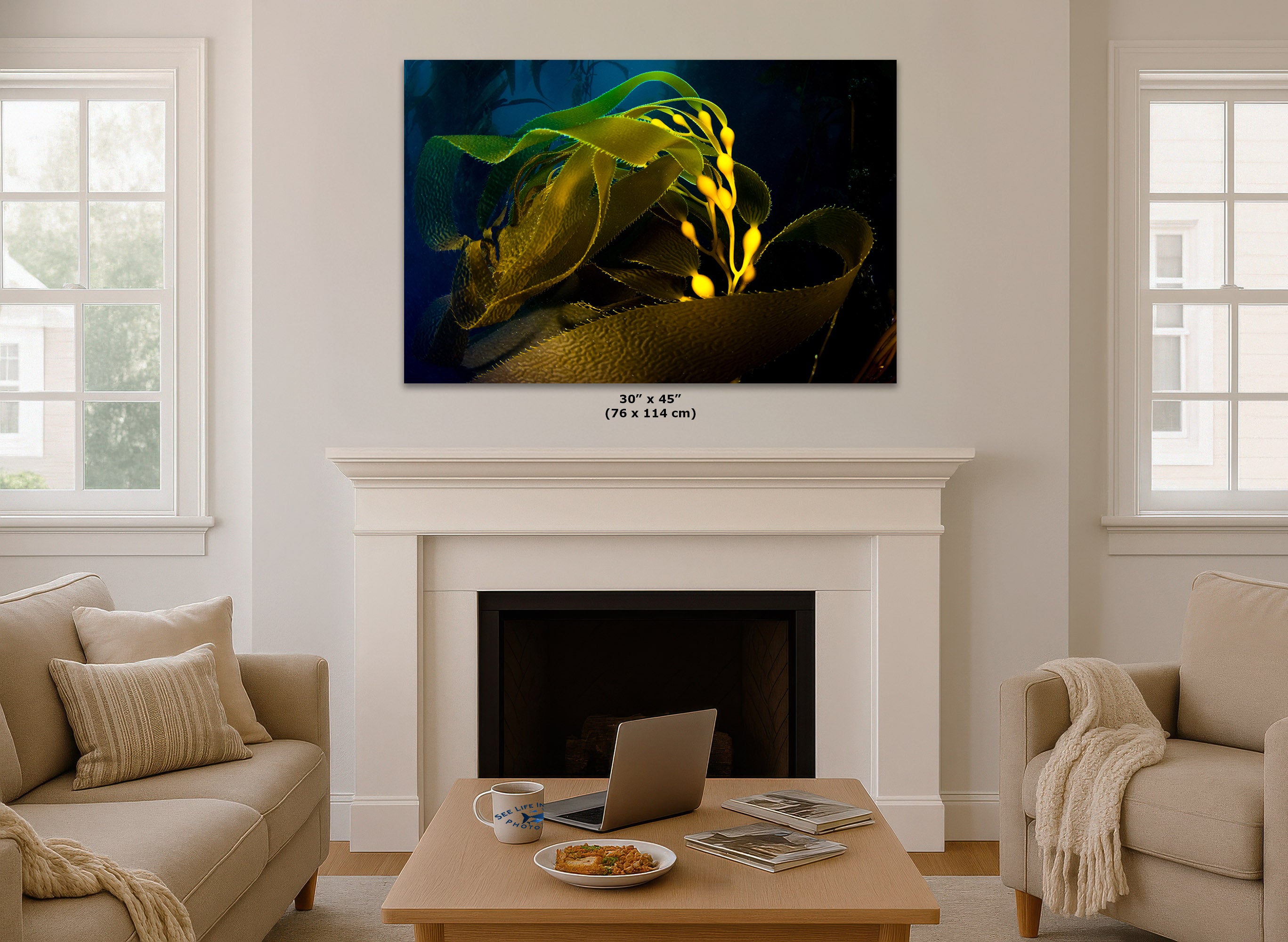 An abstract wall art print hangs above a white fireplace mantel in a bright living room. The artwork shows glowing yellow and green abstract forms against a dark blue background.