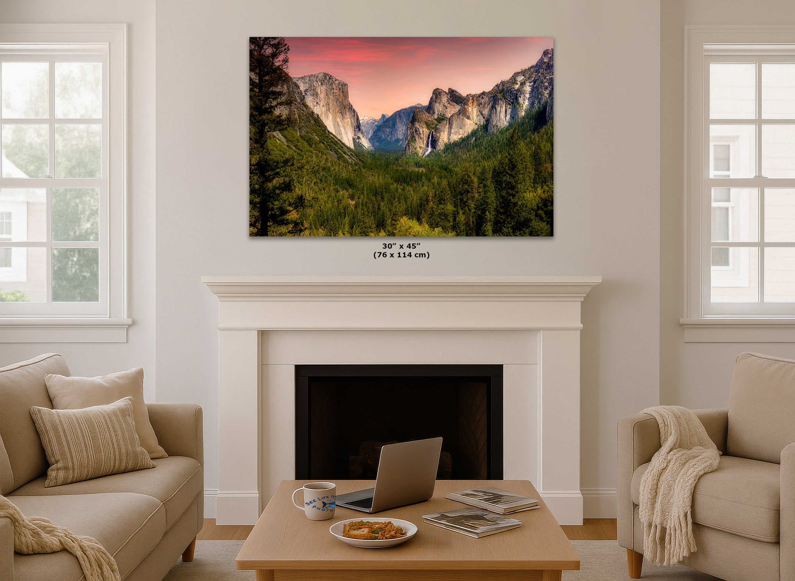 A wall art print showing a mountain valley landscape at sunset, displayed above a white fireplace mantel in a bright living room. Small text below the print indicates dimensions 30 x 45 in (76 x 114 cm).
