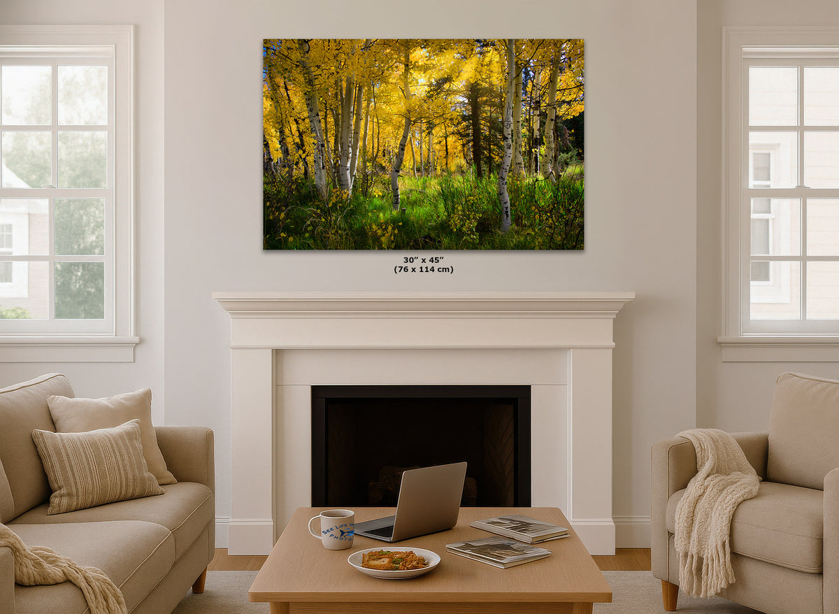 A wall art print showing a golden autumn forest hangs above a white fireplace mantel in a bright living room. The print depicts yellow and green trees with brown trunks.