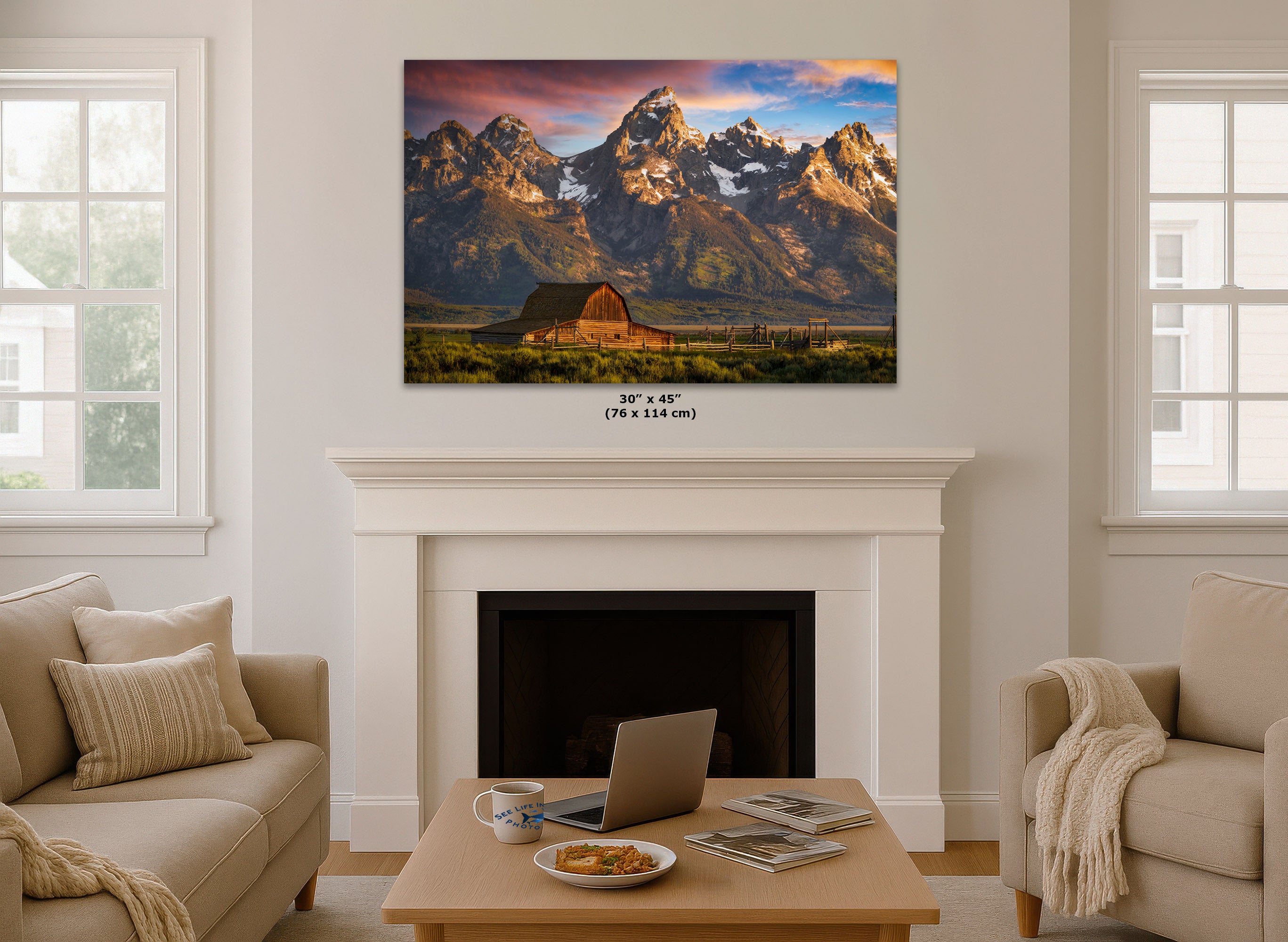 A wall art print showing a mountain landscape with a barn is displayed above a white fireplace in a styled living room. The print includes size text below it reading 30 x 45 in (76 x 114 cm).