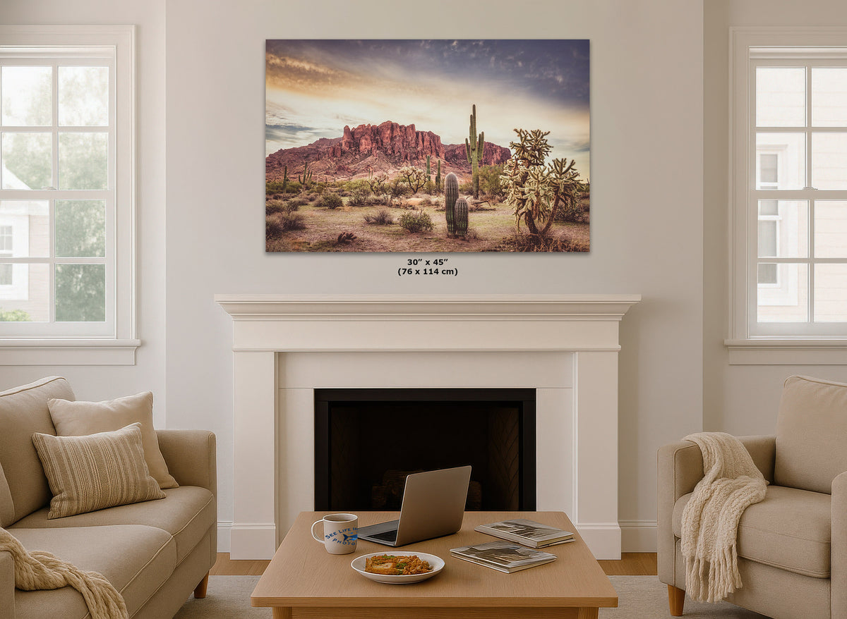 A desert landscape wall art print hangs above a white fireplace mantel in a bright living room. The artwork shows red rock desert mountains, cacti, and shrubs under a dramatic sky.