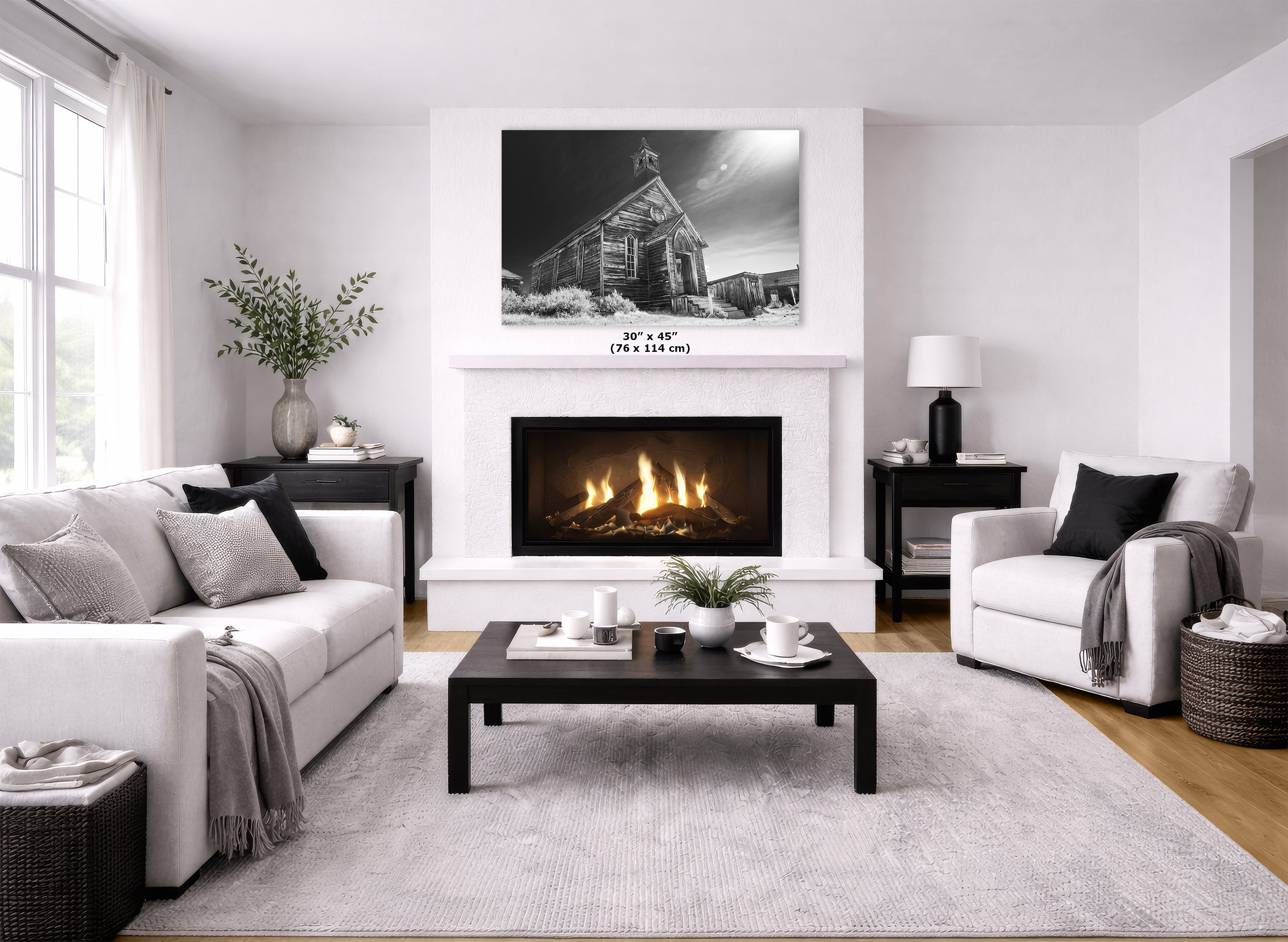 A modern living room featuring a large black and white wall art print of a church building above a white fireplace. The room is styled with a white sofa, a white armchair, a dark wood coffee table, and a light gray textured rug.