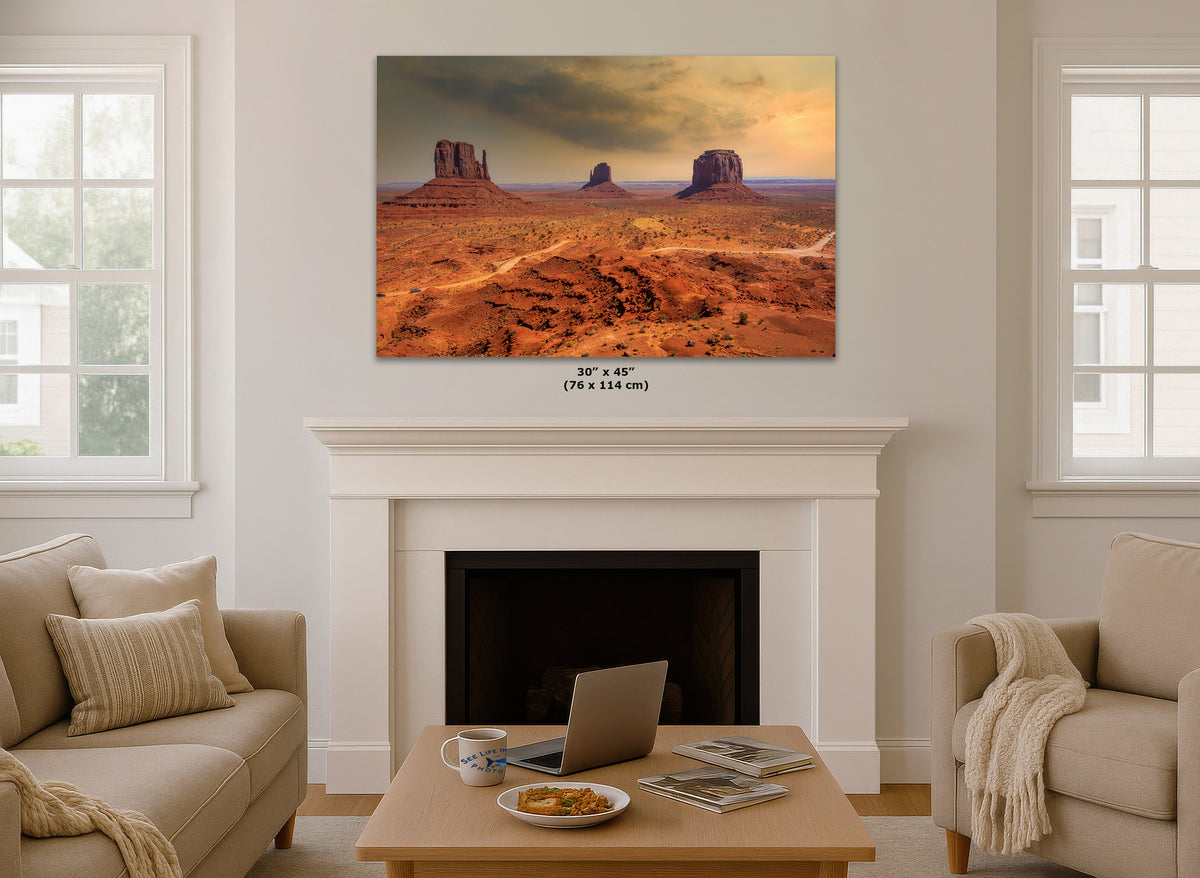 A wall art print depicting a desert landscape with buttes under a dramatic sky, displayed above a white fireplace mantel in a bright living room. Small text below the print reads 30 x 45 (76 x 114 cm).
