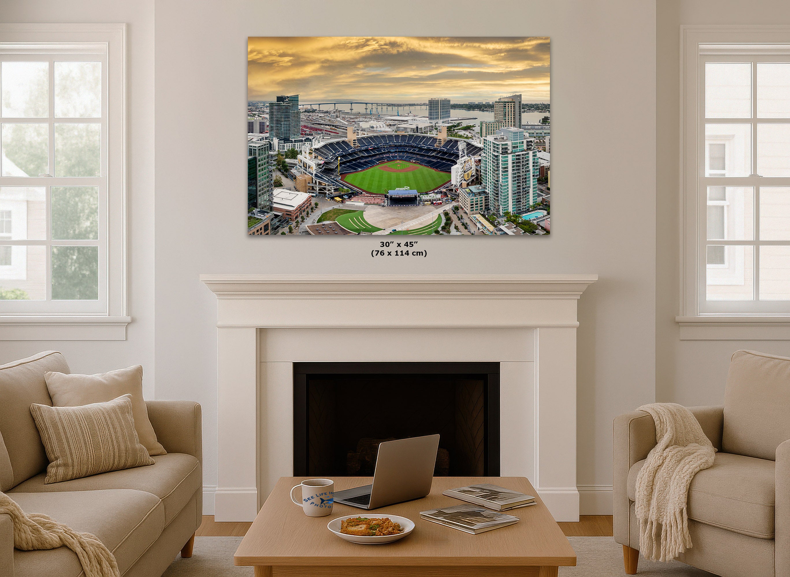 A 30" x 45" canvas print of an aerial stadium view at sunset, displayed on a white fireplace mantel in a modern living room setting.