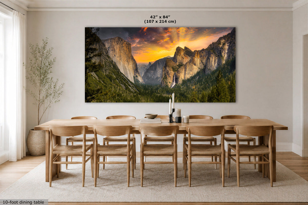 A large Yosemite Tunnel View wall art print showing a mountain valley landscape at sunset, displayed above a wooden dining table and chairs in a bright dining room. The print includes size text reading 42 x 84 in (107 x 214 cm).