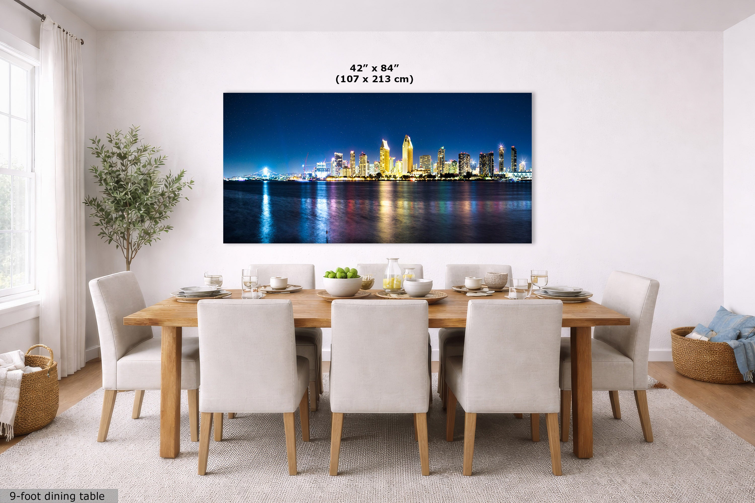 A large rectangular wall art print showing a nighttime city skyline reflected on water, displayed above a dining table in a bright modern dining room. Text above the print reads 42 x 84" (107 x 213 cm).
