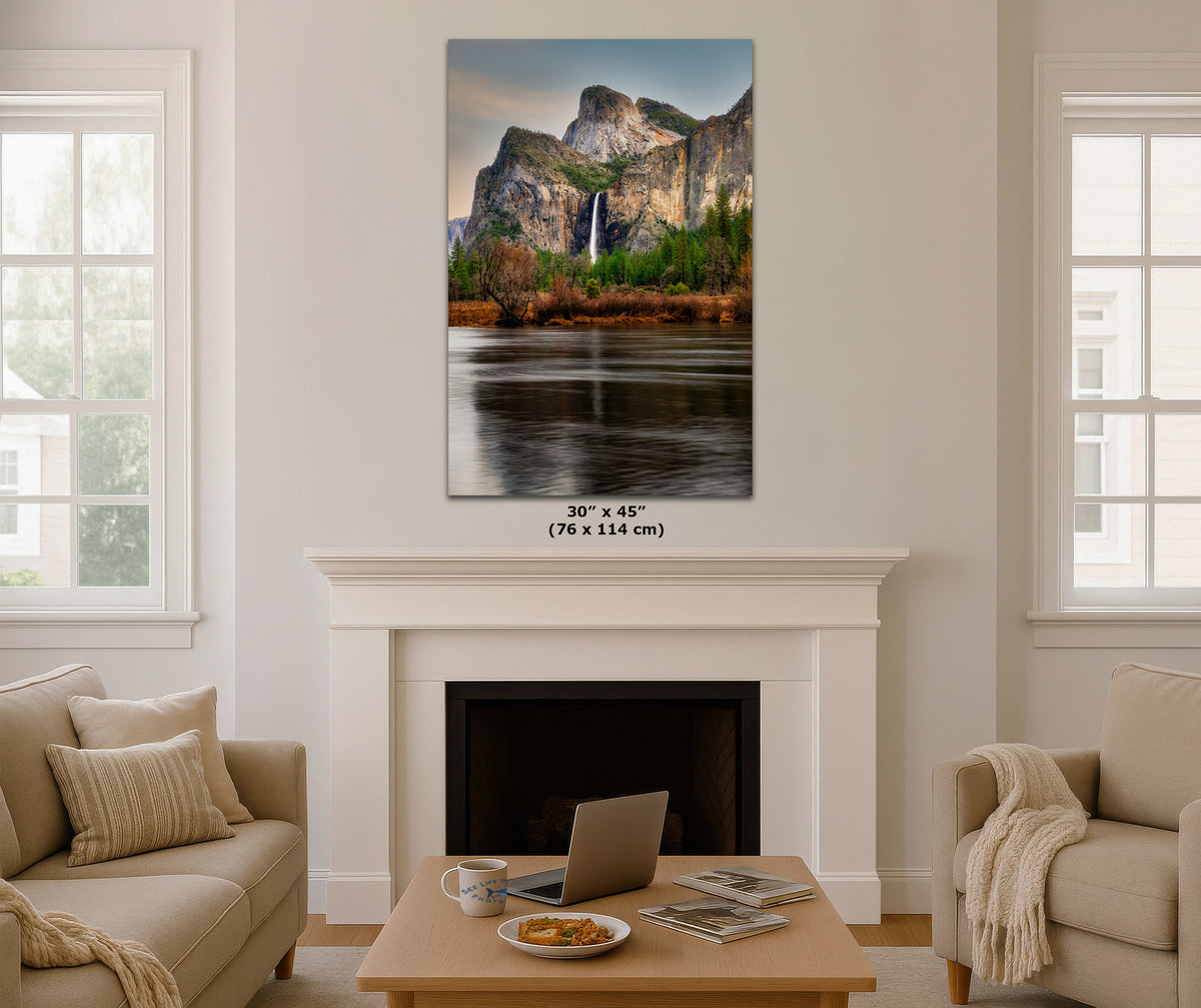A vertical canvas print of Bridalveil Falls in Yosemite National Park, 30" x 45" (76 x 114 cm), displayed on a white wall above a fireplace in a modern, neutral-toned living room setting.