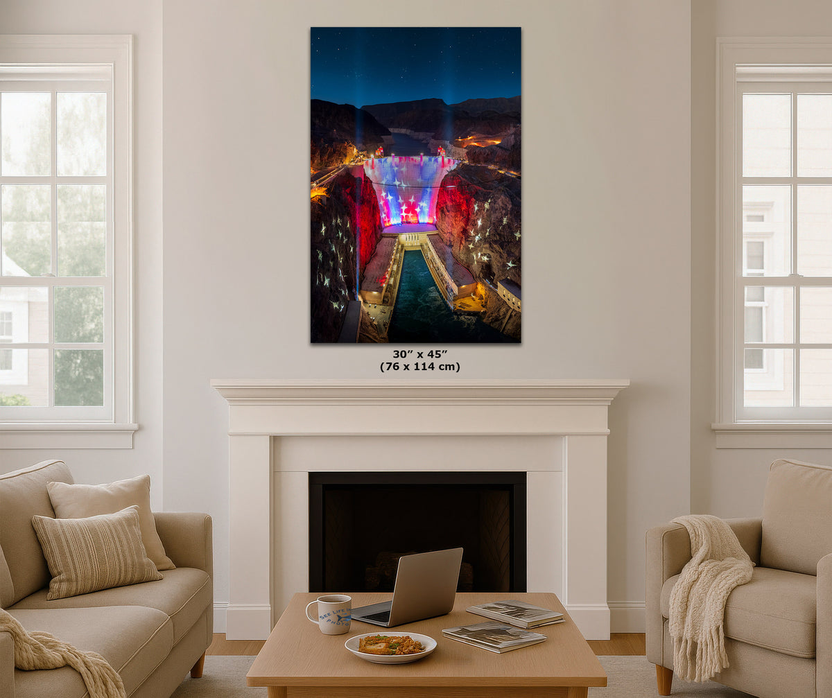 A vertical wall art print showing a brightly lit dam and canyon scene, displayed above a white fireplace in a styled living room with beige sofas, a coffee table, and windows. The print includes size text below it reading 30 x 45 (76 x 114 cm).