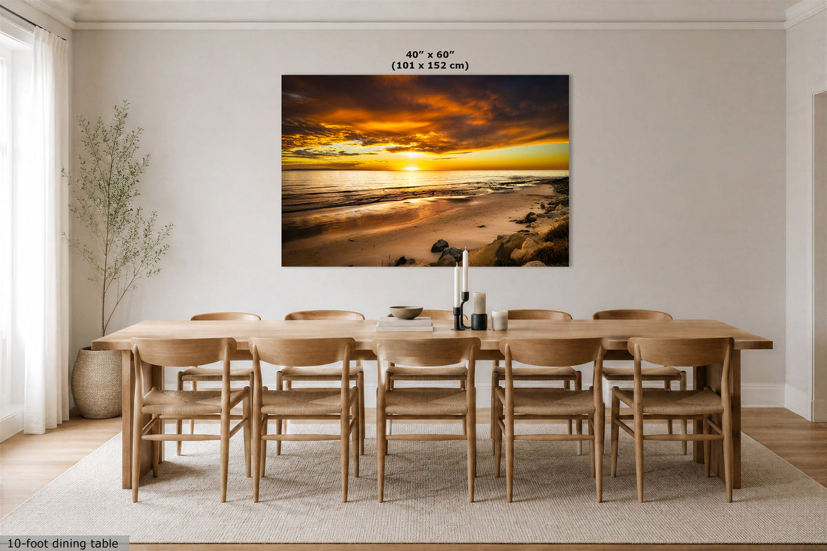 A large rectangular wall art print showing a dramatic beach sunset, displayed above a wooden dining table and chairs in a bright modern dining room. The print includes size text at the top reading 40" x 60" (101 x 152 cm).