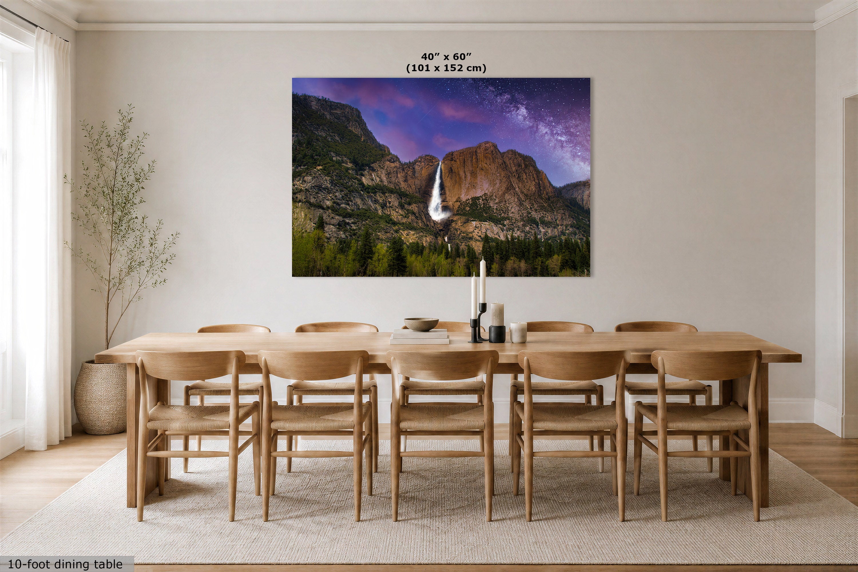 A large rectangular wall art print showing a mountain landscape with a waterfall and purple sky, displayed above a wooden dining table and chairs in a bright dining room. Text at the top reads 40" x 60" (101 x 152 cm).